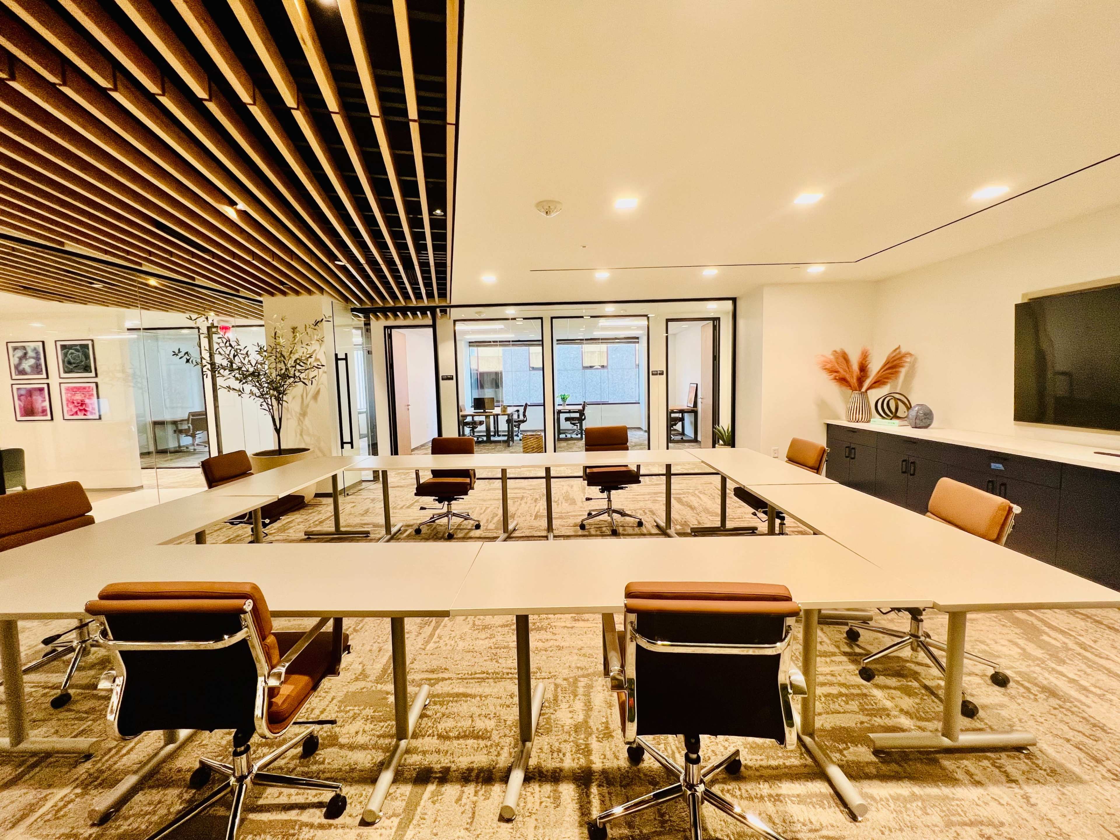 A modern conference room with a large rectangular table surrounded by ergonomic chairs and glass partitions leading to other meeting areas.
