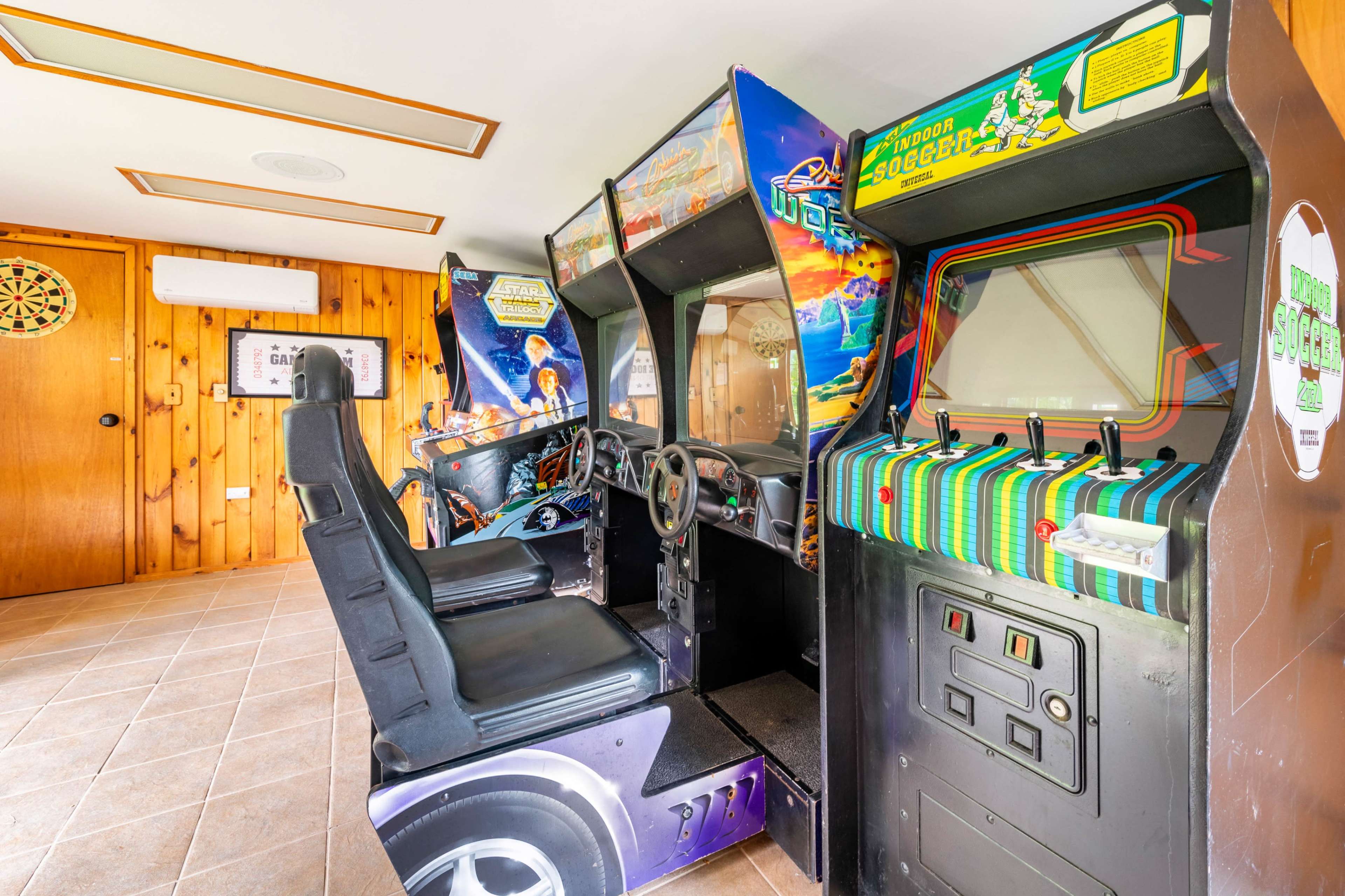 The image shows a retro arcade game cabinet positioned in a room with wooden paneling and tile flooring.