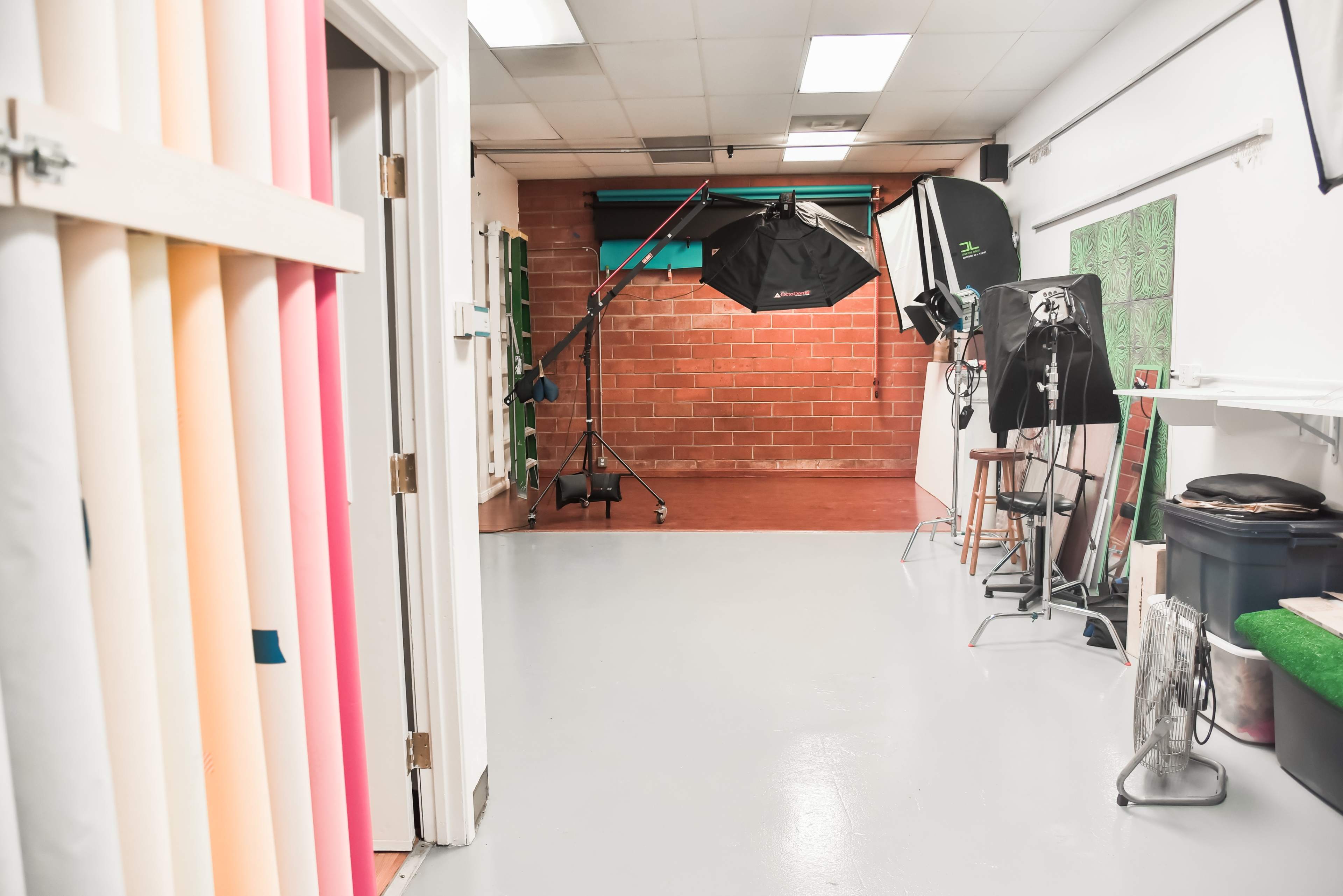 A photography studio with colored backdrops, lighting equipment, and a brick wall.