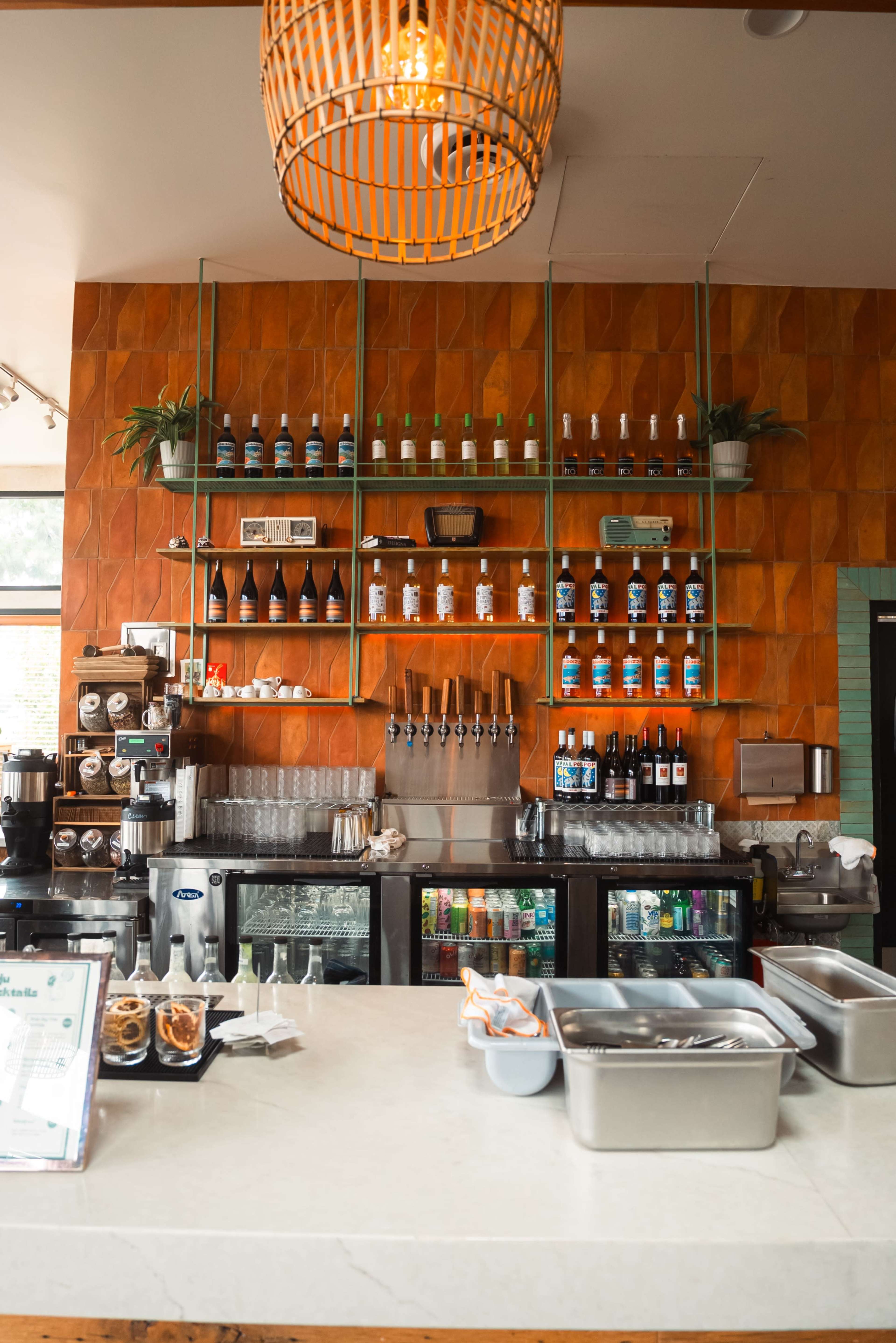 The image shows a modern coffee shop counter featuring a variety of drinks on shelves, glassware, and food containers.