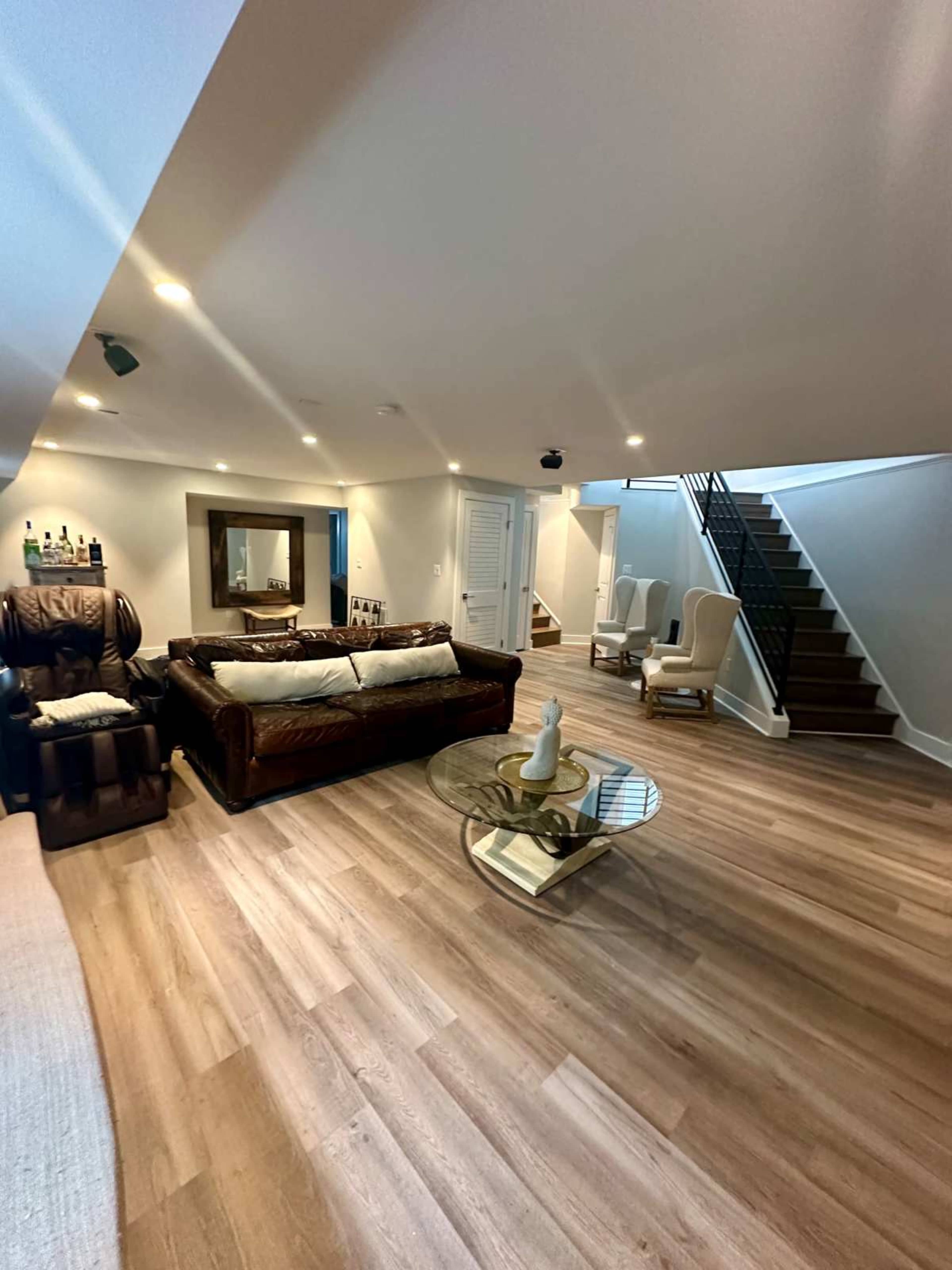 A finished basement with a sitting area featuring a leather couch, a glass coffee table, and a staircase leading to an upper level.