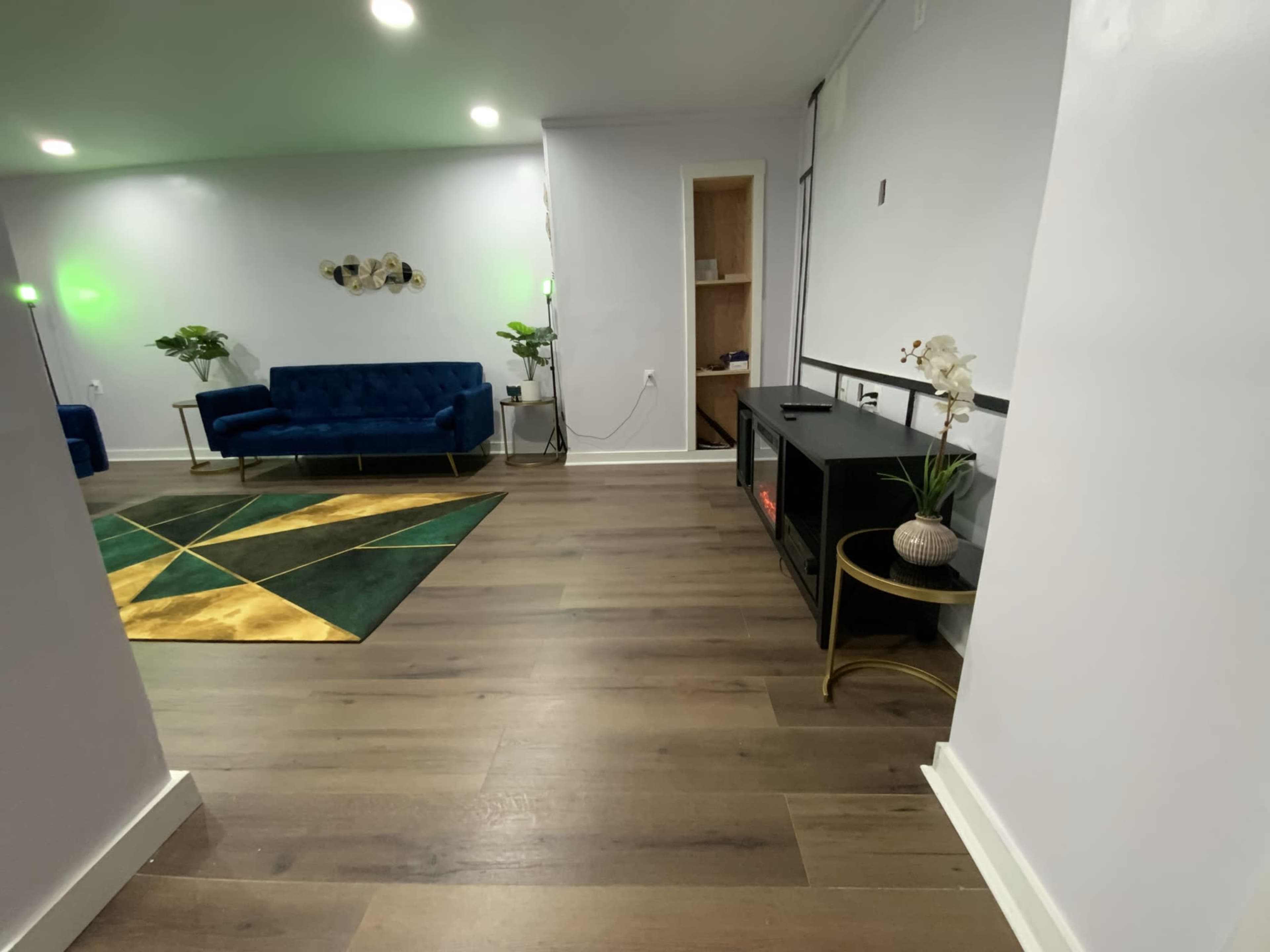 A modern interior space with a blue couch, a geometric rug, and a TV stand against a light-colored wall.