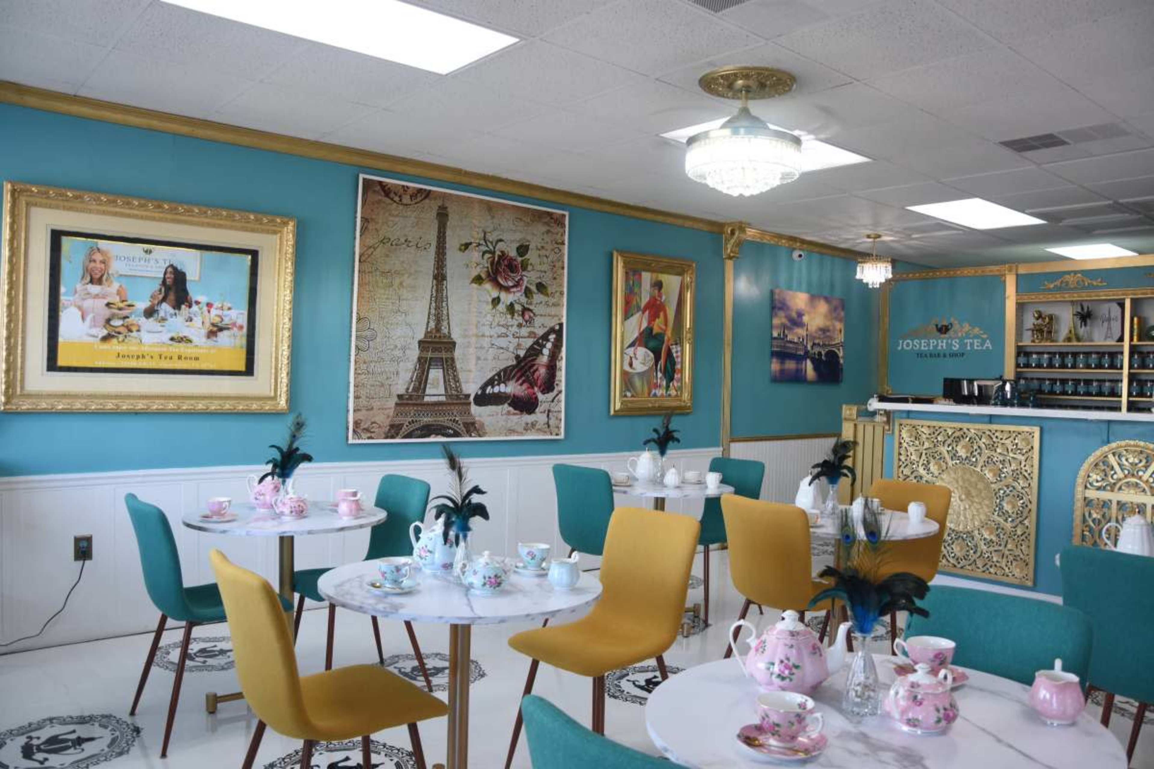 A tea room with elegantly set tables, featuring colorful chairs and ornate decorations on the walls, including artwork and a display counter.