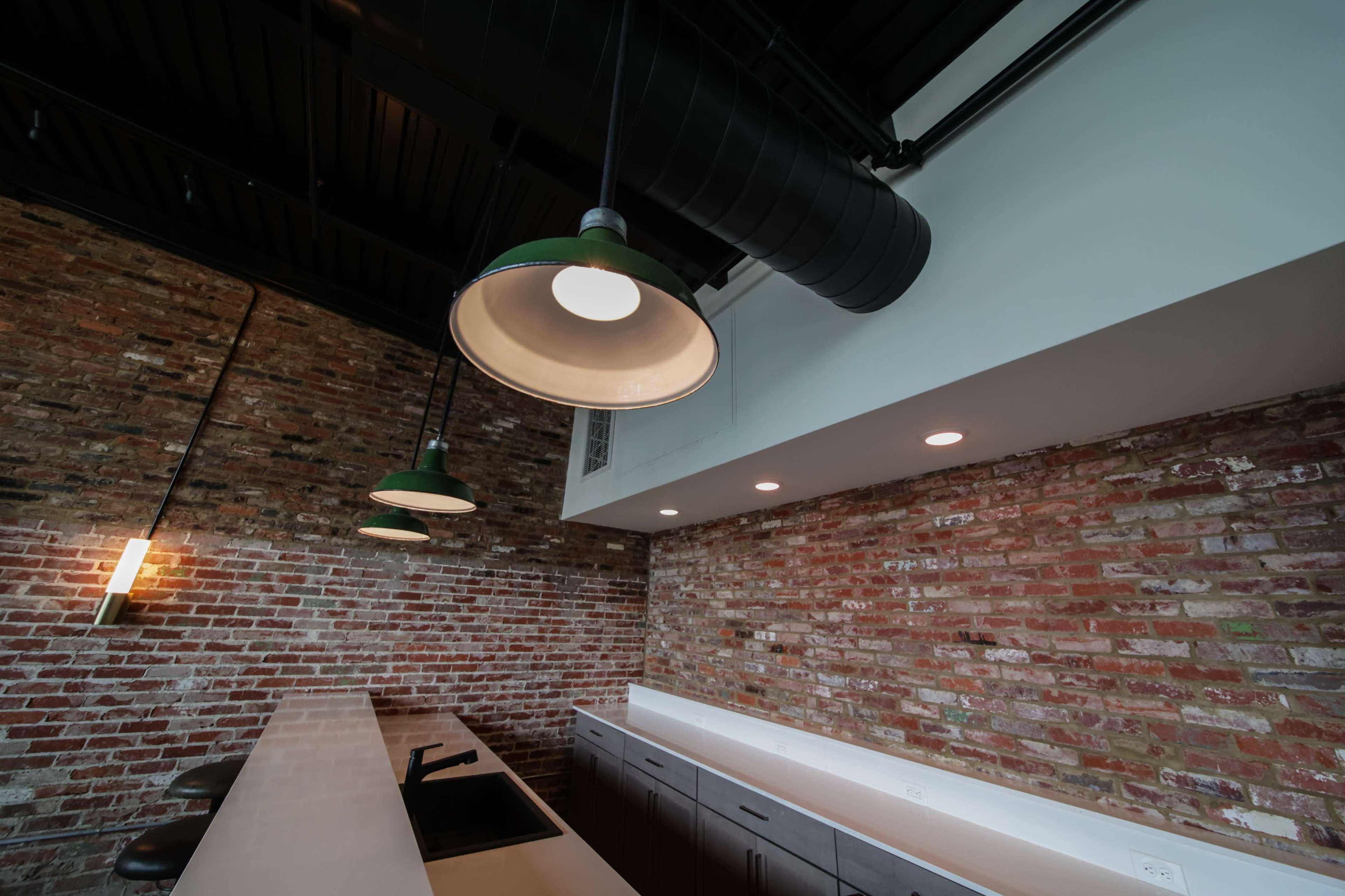 The image shows a modern kitchen space featuring exposed brick walls, a countertop, and industrial-style pendant lighting.