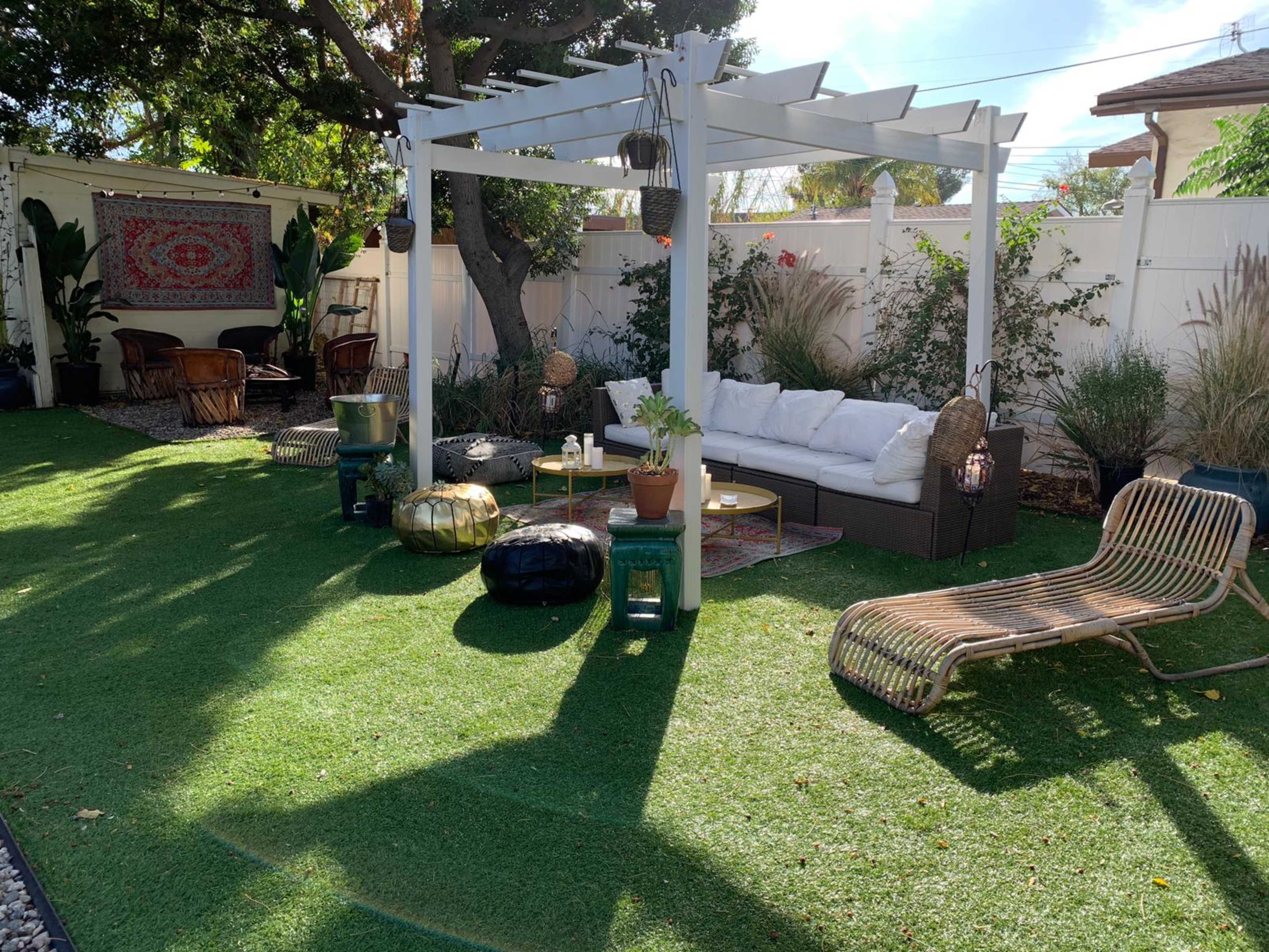 A landscaped backyard with a white pergola, outdoor seating, and various plants on artificial grass.