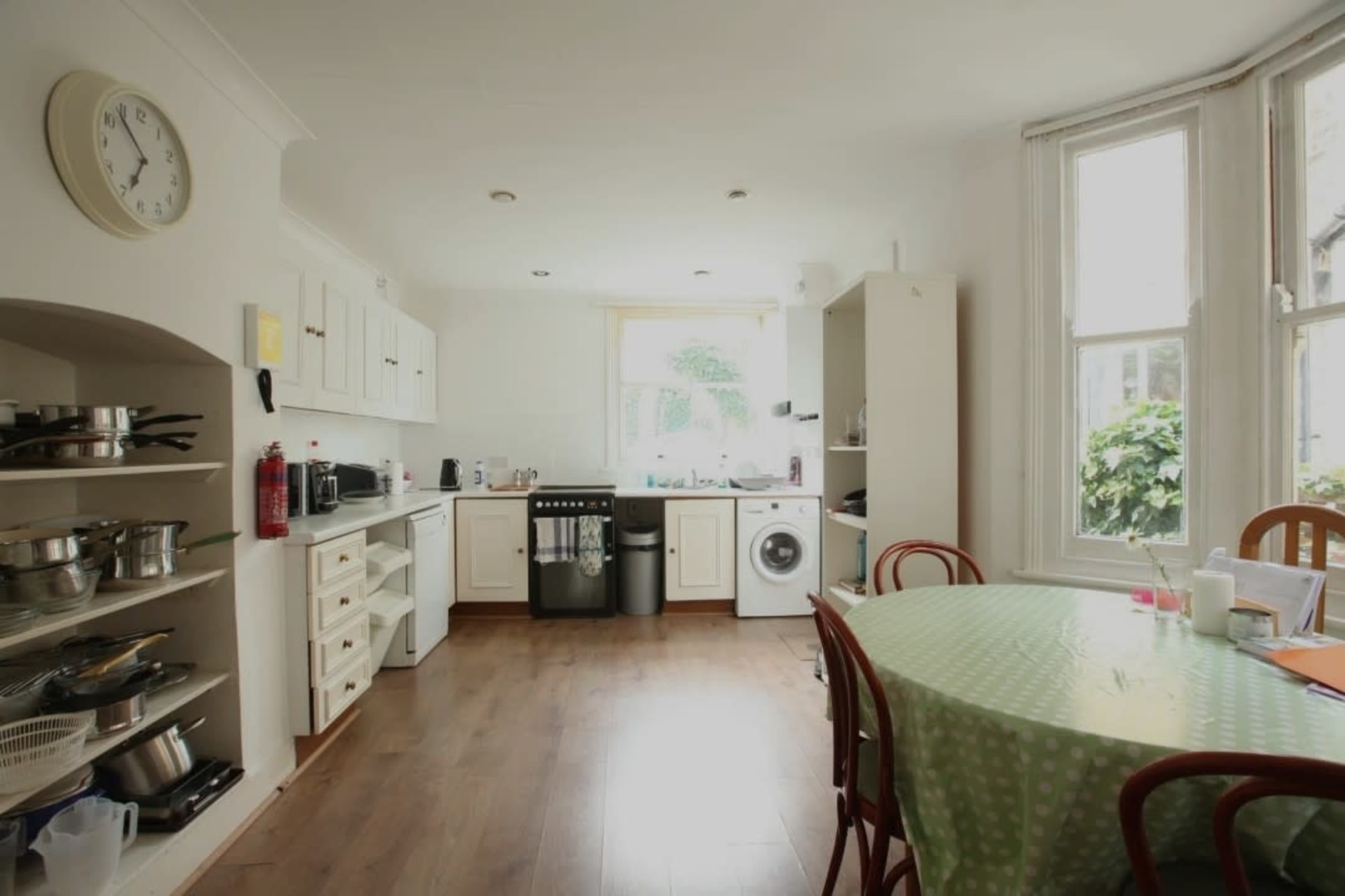 A kitchen with a dining table, and cabinets that include cookware, a washing machine, and various kitchen appliances.