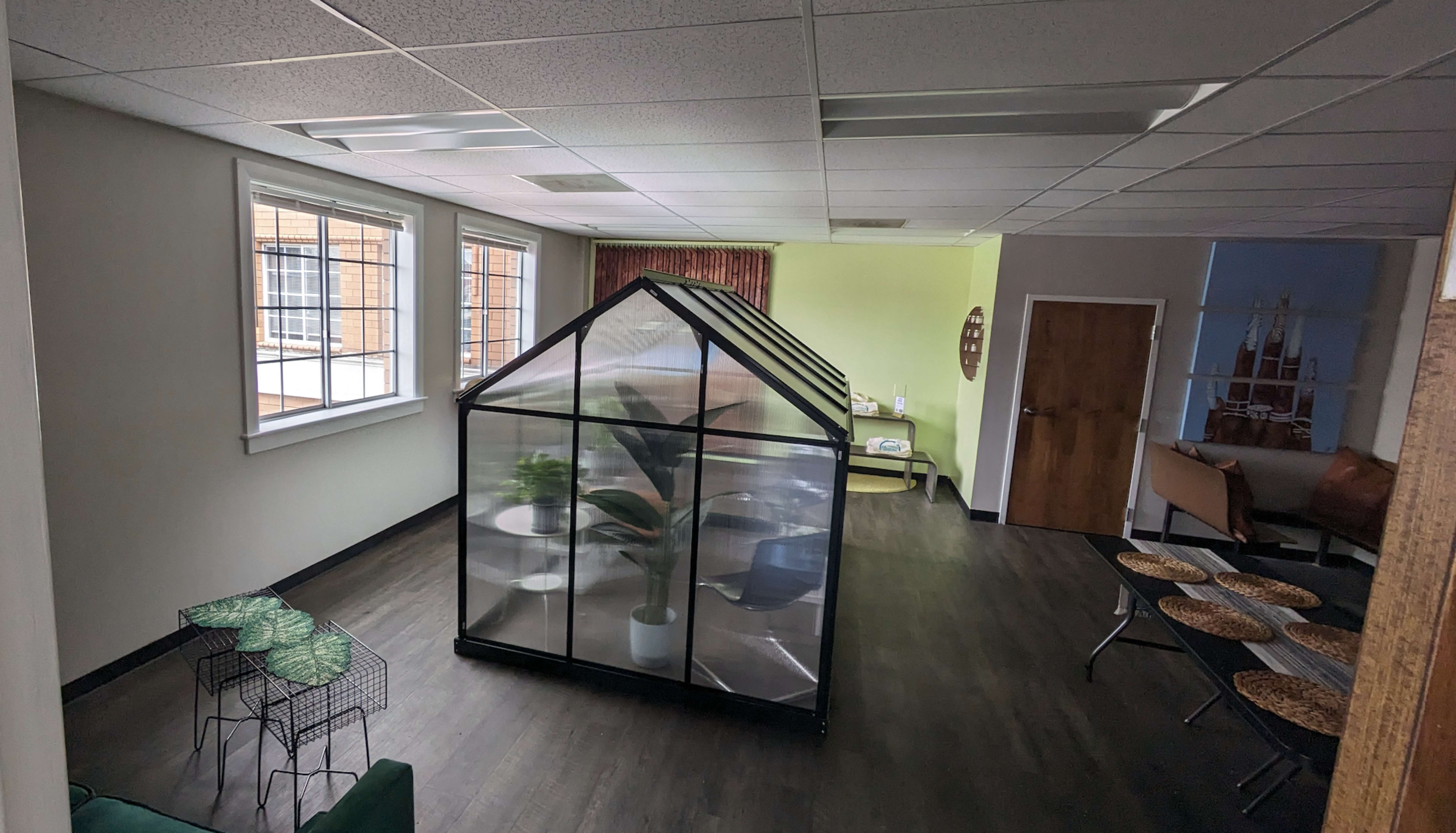 A spacious office interior featuring a glass greenhouse in the center, with seating areas and windows along the walls.
