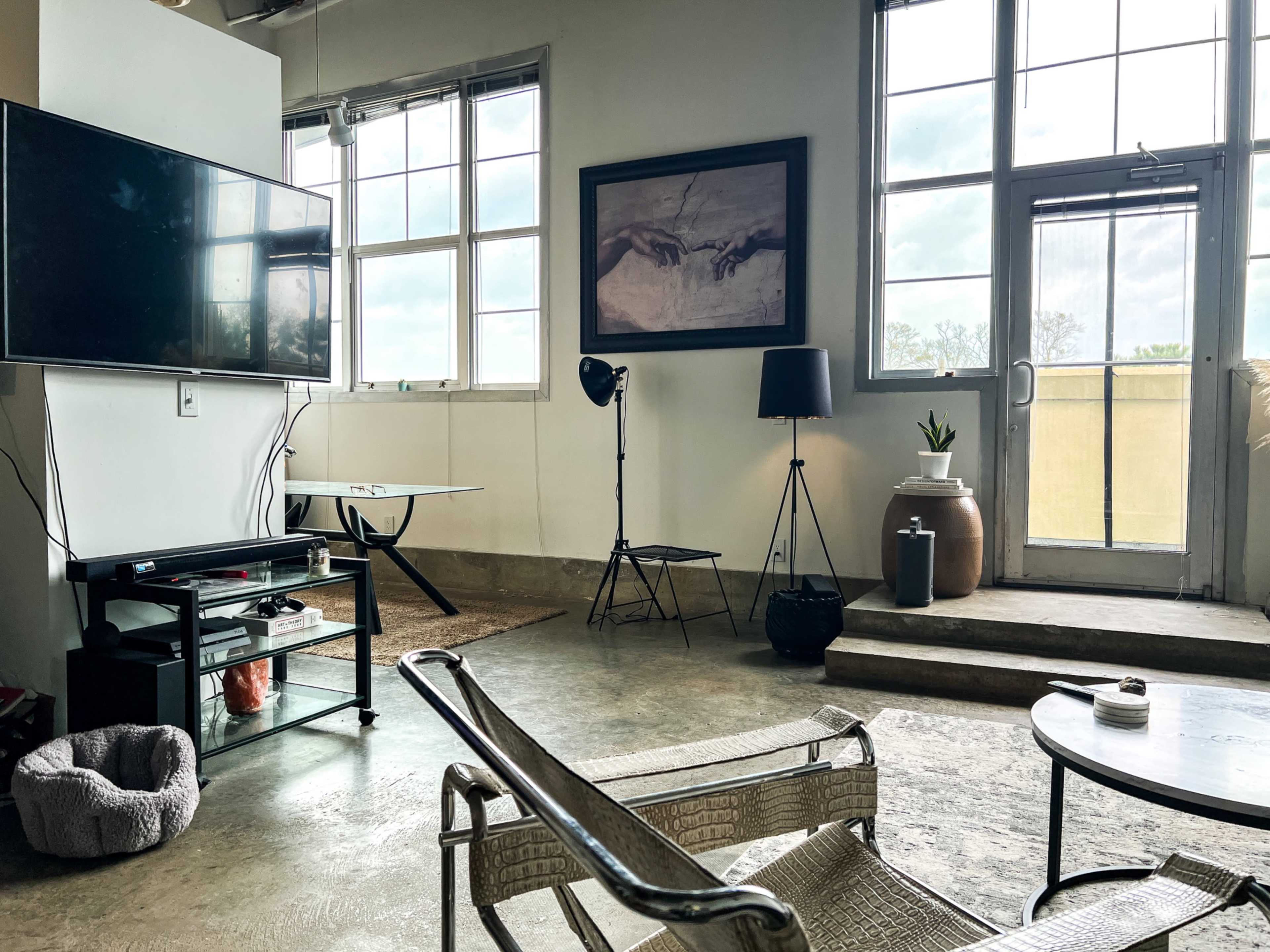 A modern interior space features a television on the wall, a coffee table, and a grey sofa, with large windows letting in natural light.