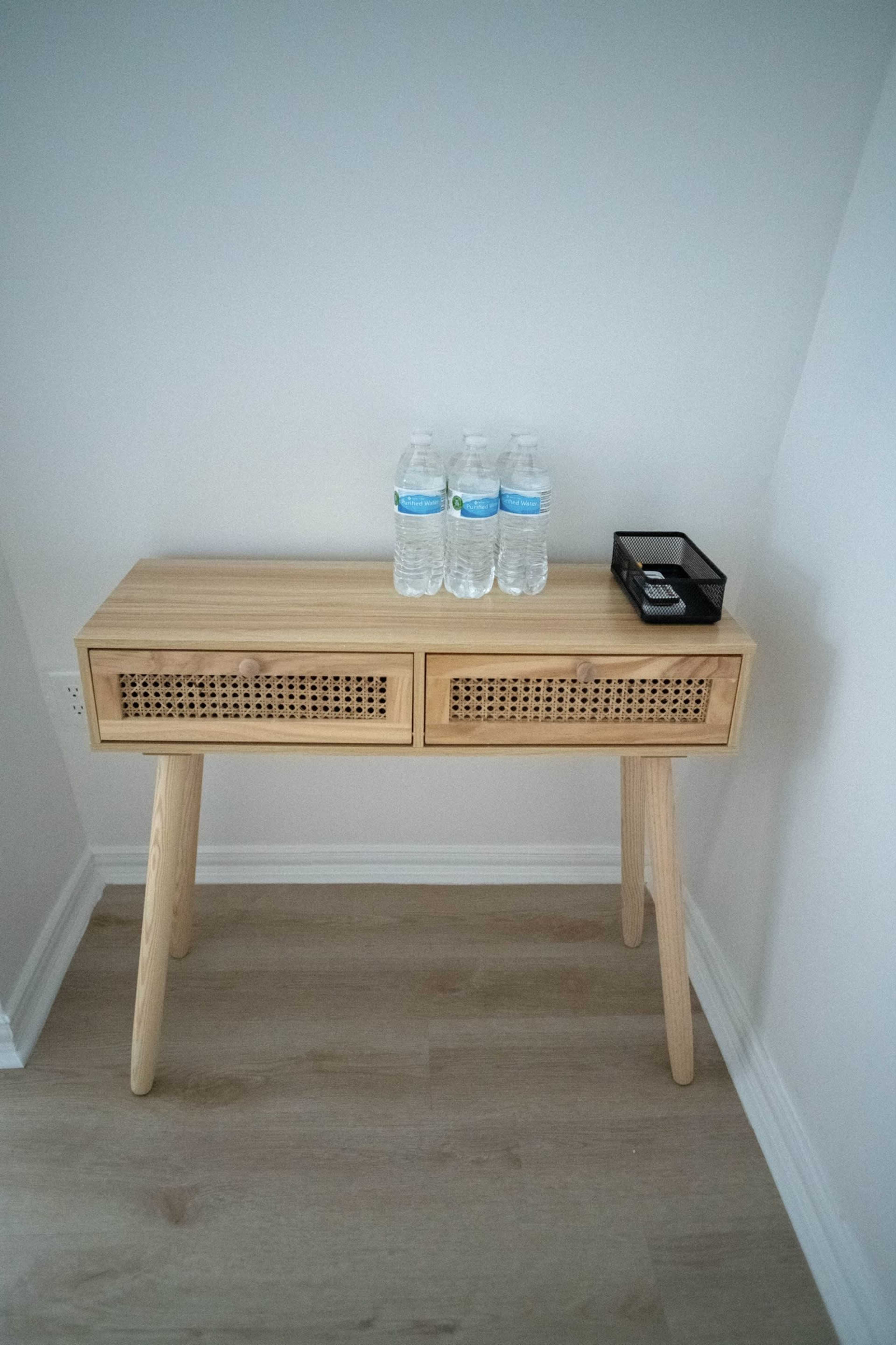 A wooden console table with two drawers stands against a wall, holding three bottles of water and a small black container.