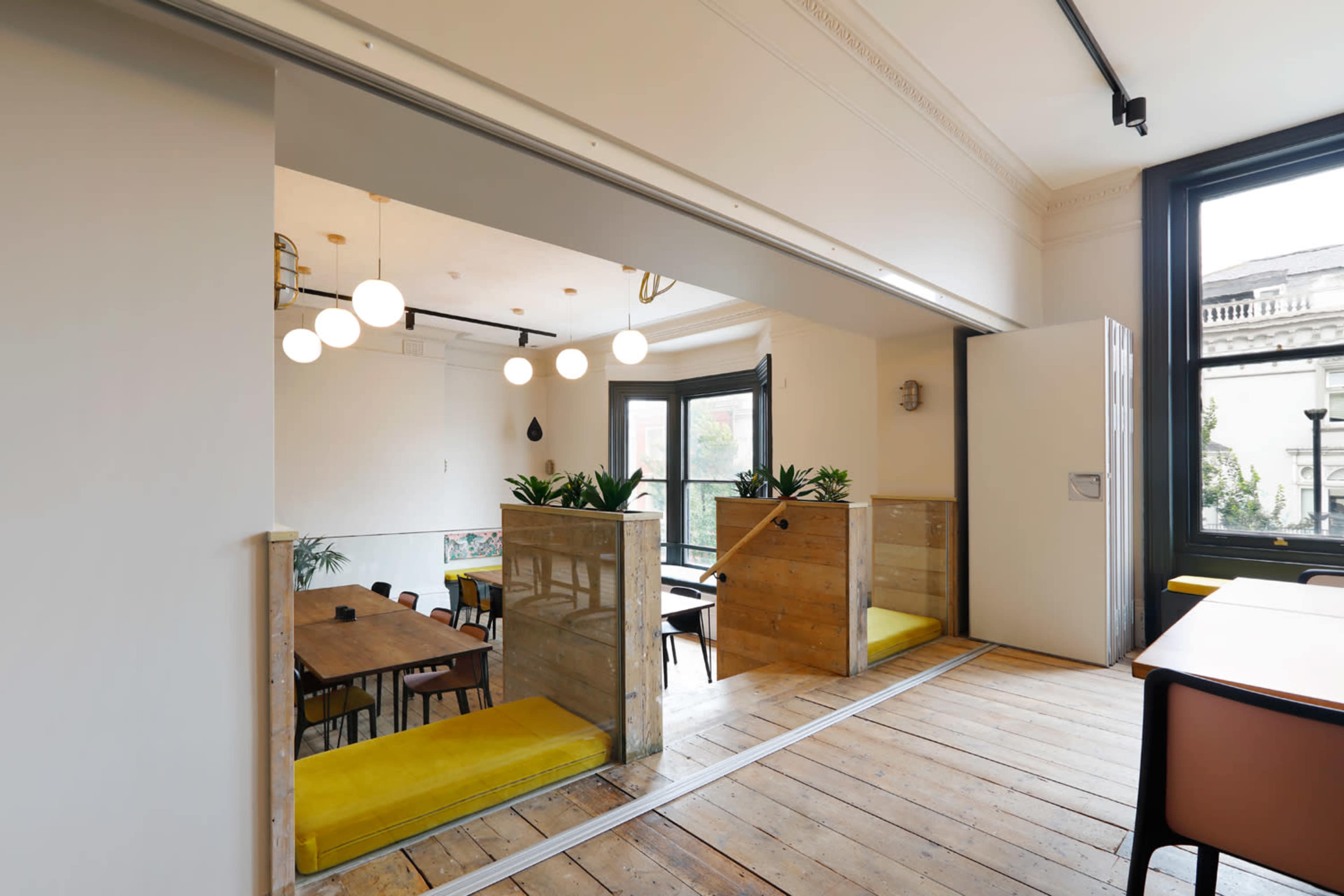 A modern, open-plan interior with wooden flooring and seating areas separated by wooden partitions.