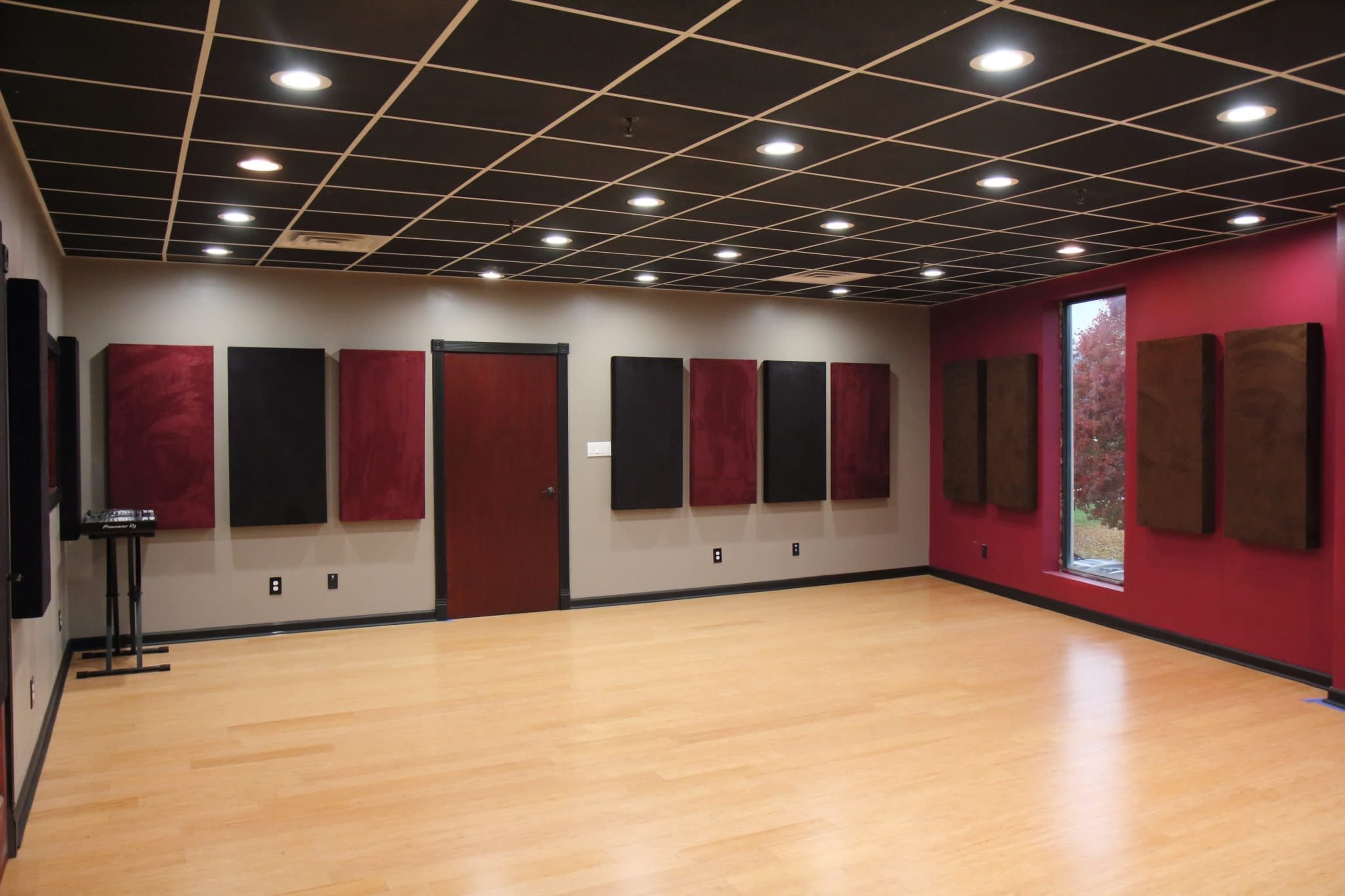 A soundproof room with black and maroon walls, wooden flooring, and several mounted acoustic panels.