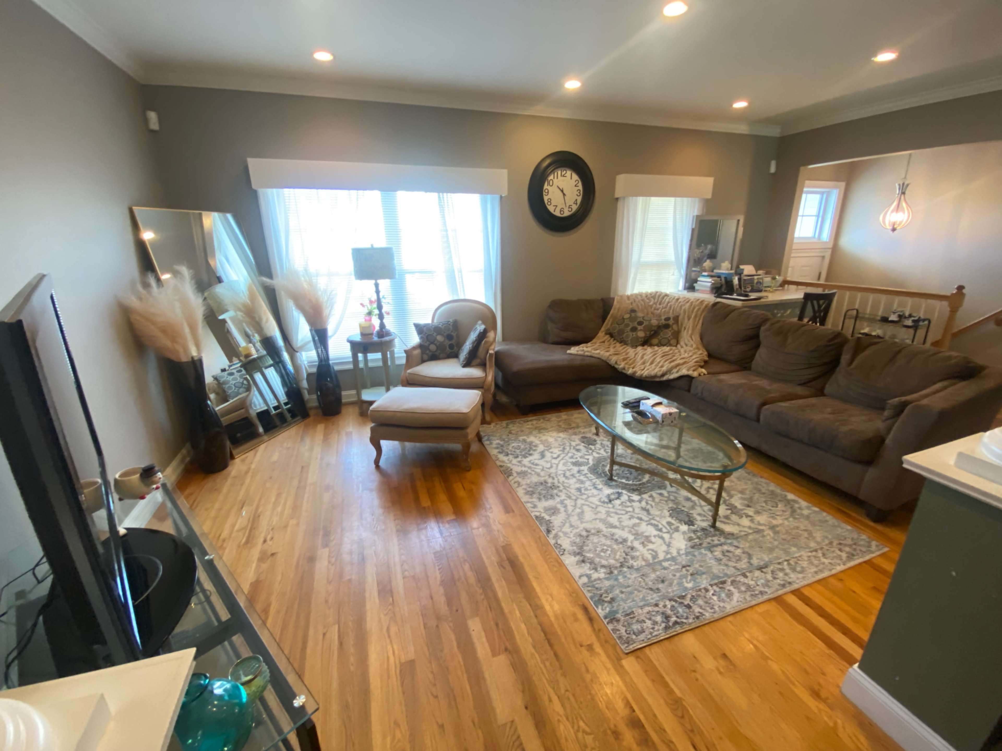 The living room features a large sectional sofa, a glass coffee table, and a decorative area rug, with natural light coming through two windows.