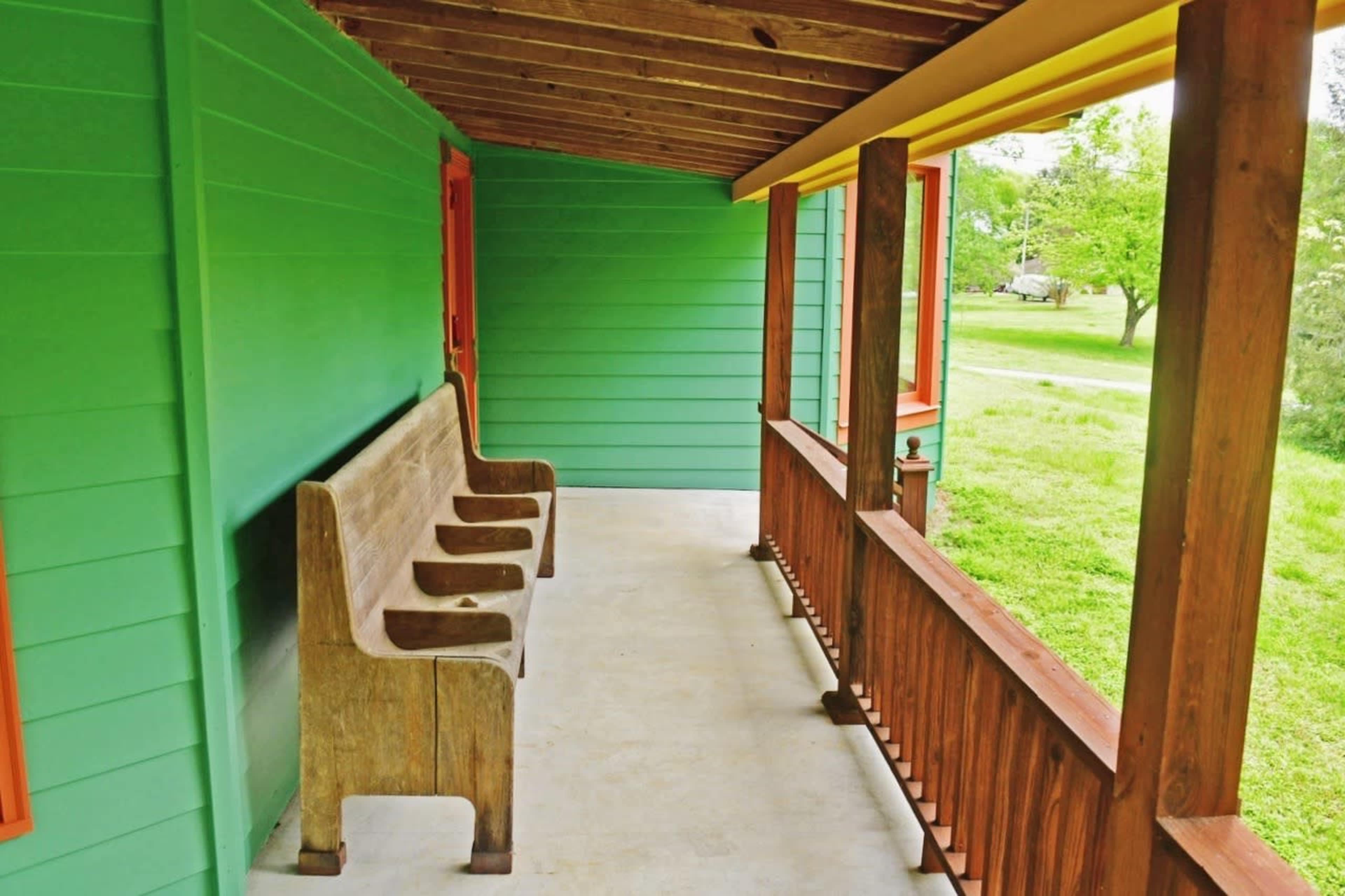 A green-painted porch with a wooden bench and a view of a grassy area outside.
