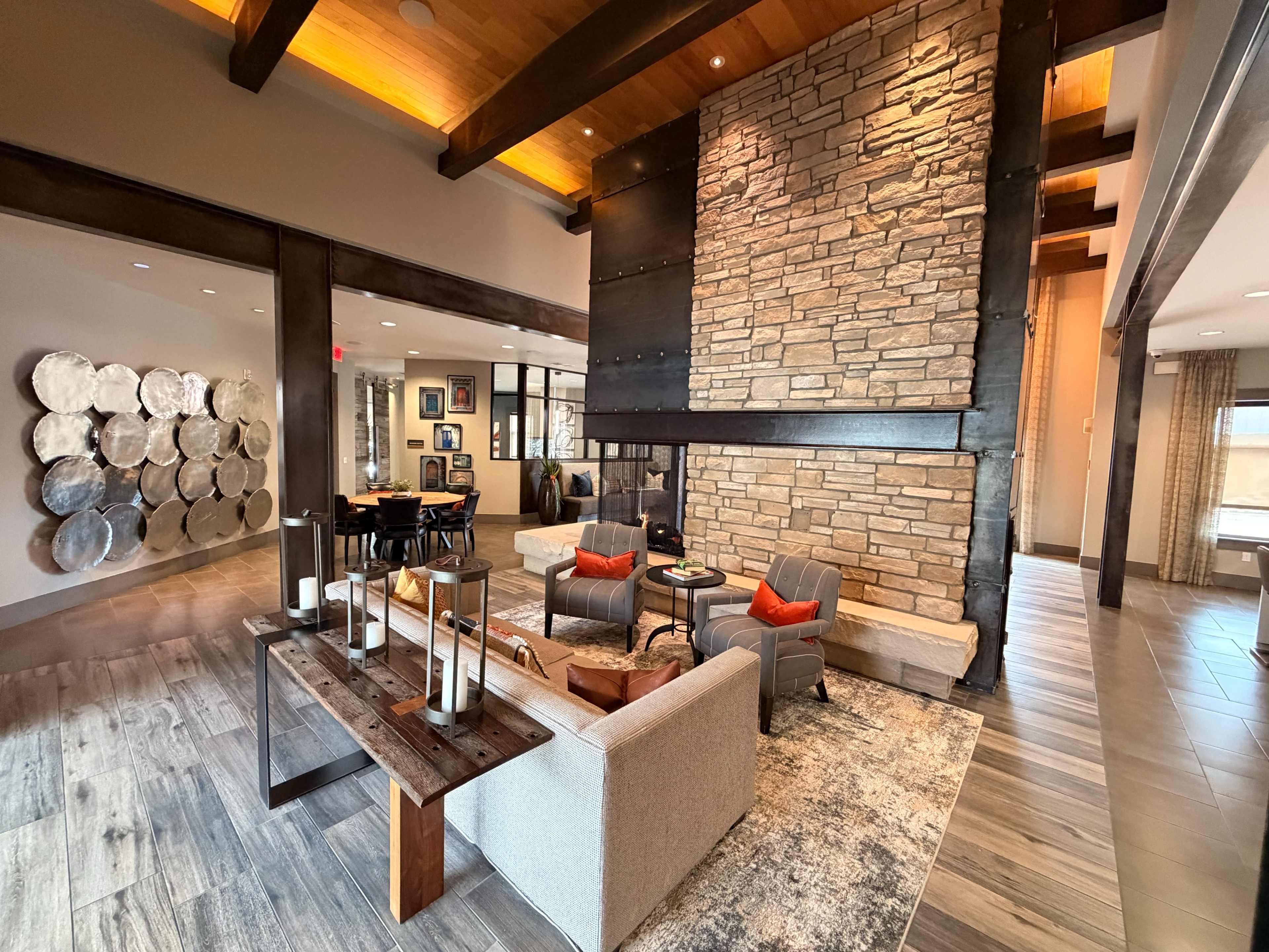 The image features a spacious living area with a stone wall, wooden beams, comfortable seating, and modern décor.