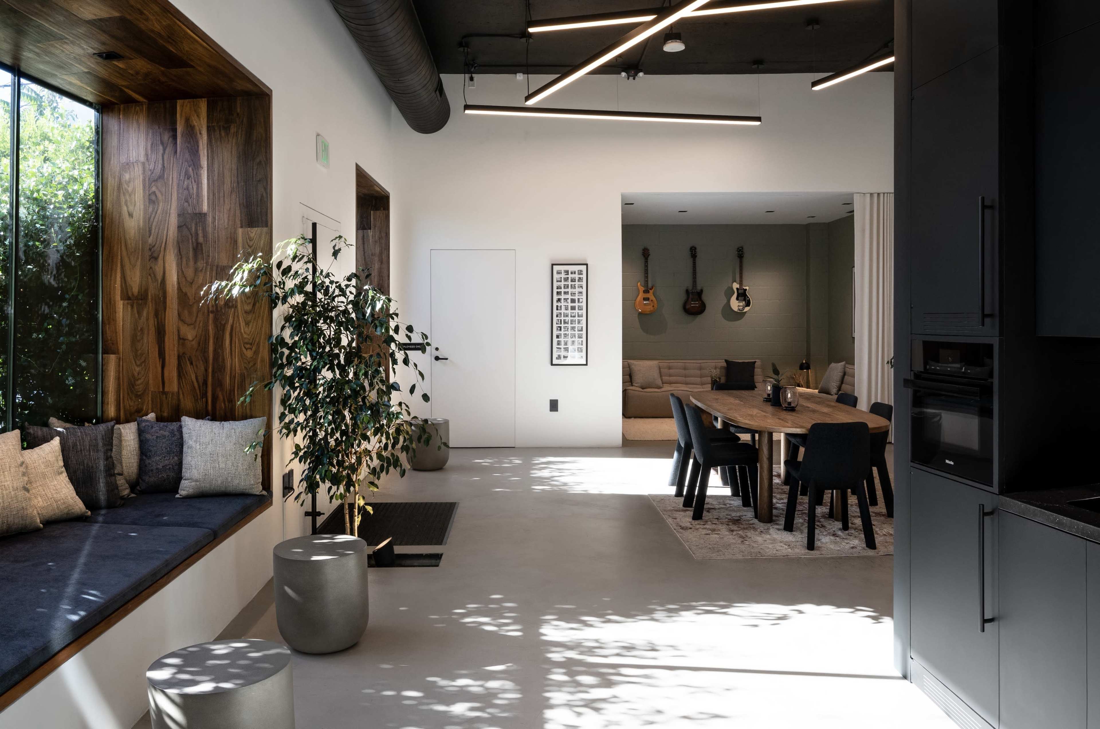 The image shows a modern interior space featuring a cozy seating area by a window, a dining table, and a lounge area with guitars on the wall.