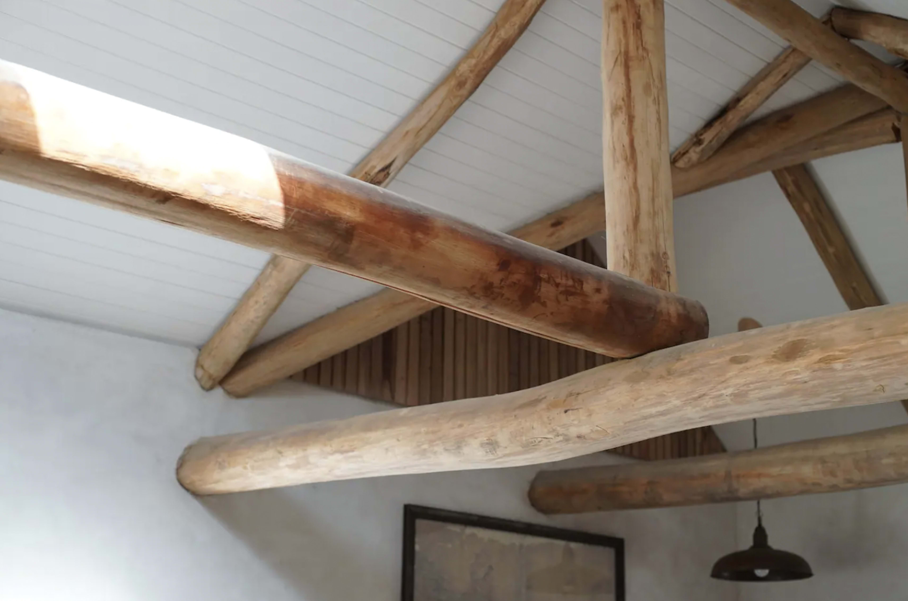 A wooden beam ceiling with exposed log supports in a room featuring a neutral color palette.