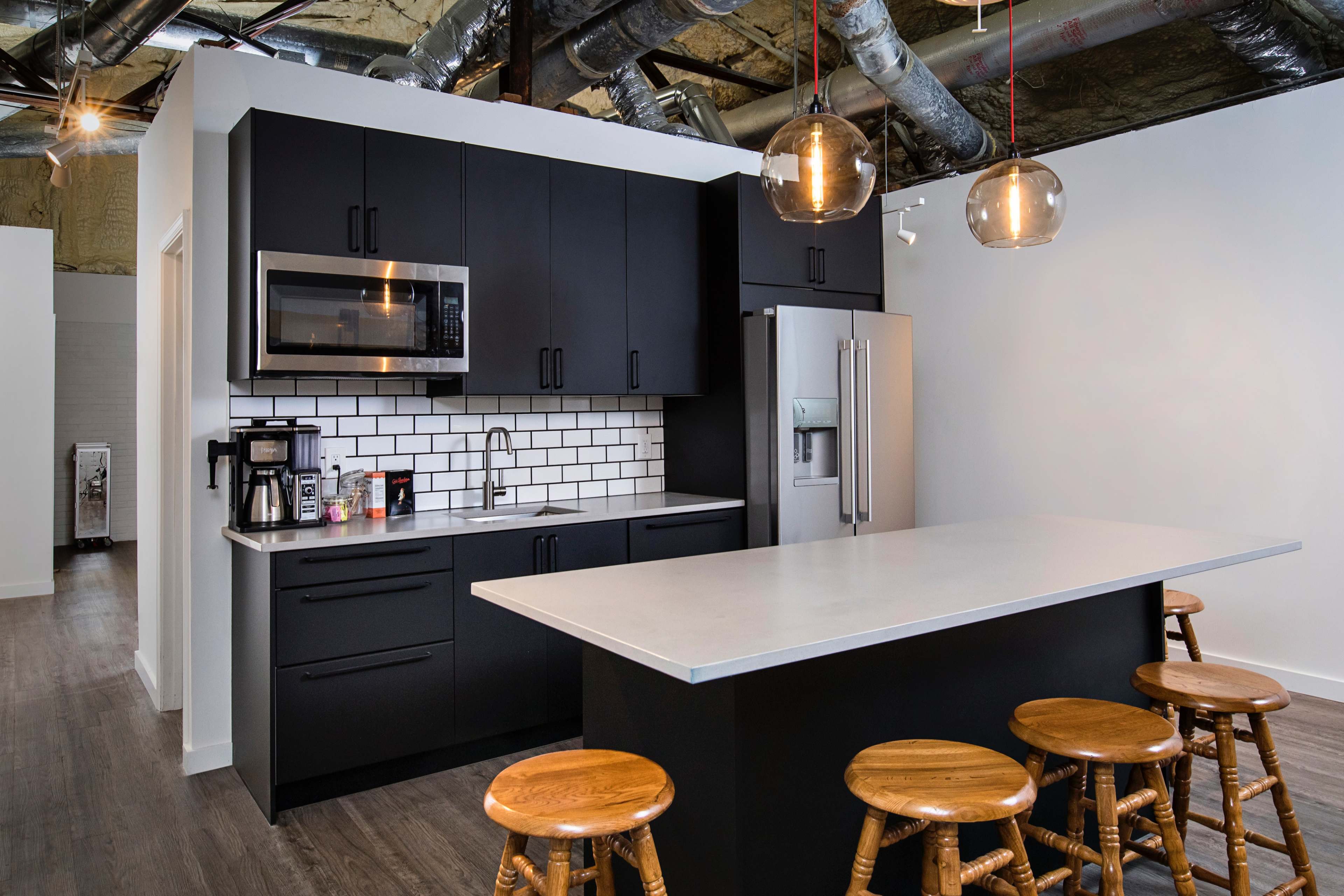 A modern kitchen with black cabinets, stainless steel appliances, a white countertop, and wooden stools arranged around a kitchen island.