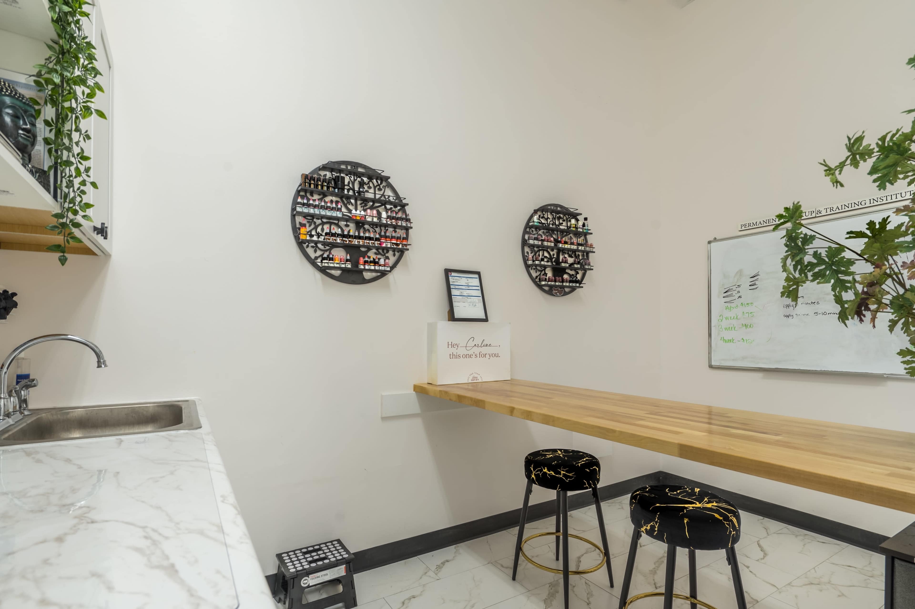 The image shows a minimalist room with a wooden table, two black stools, a sink, and wall-mounted displays of nail polish.