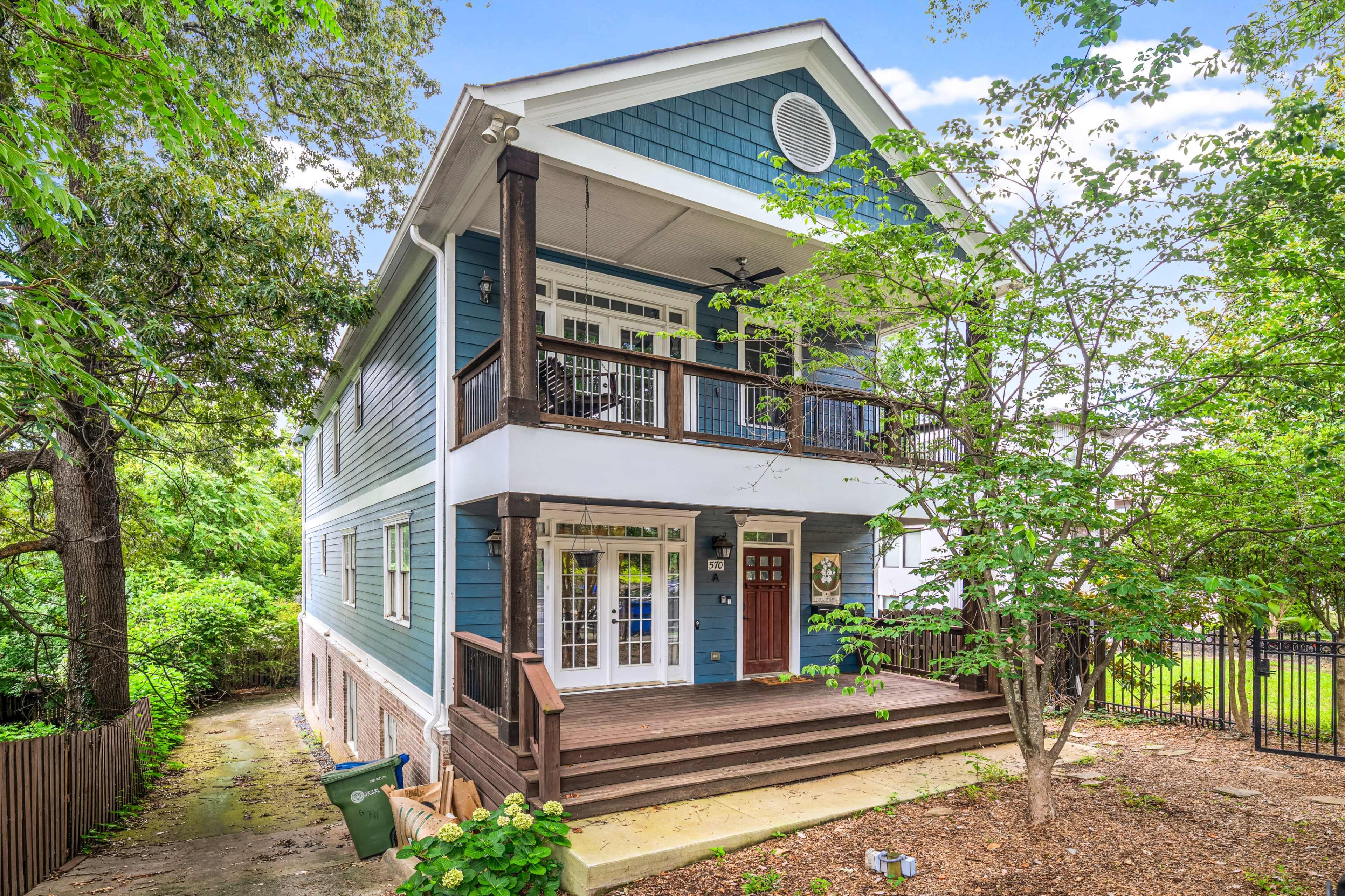 The image shows a two-story blue house with a front porch, surrounded by trees and a landscaped yard.