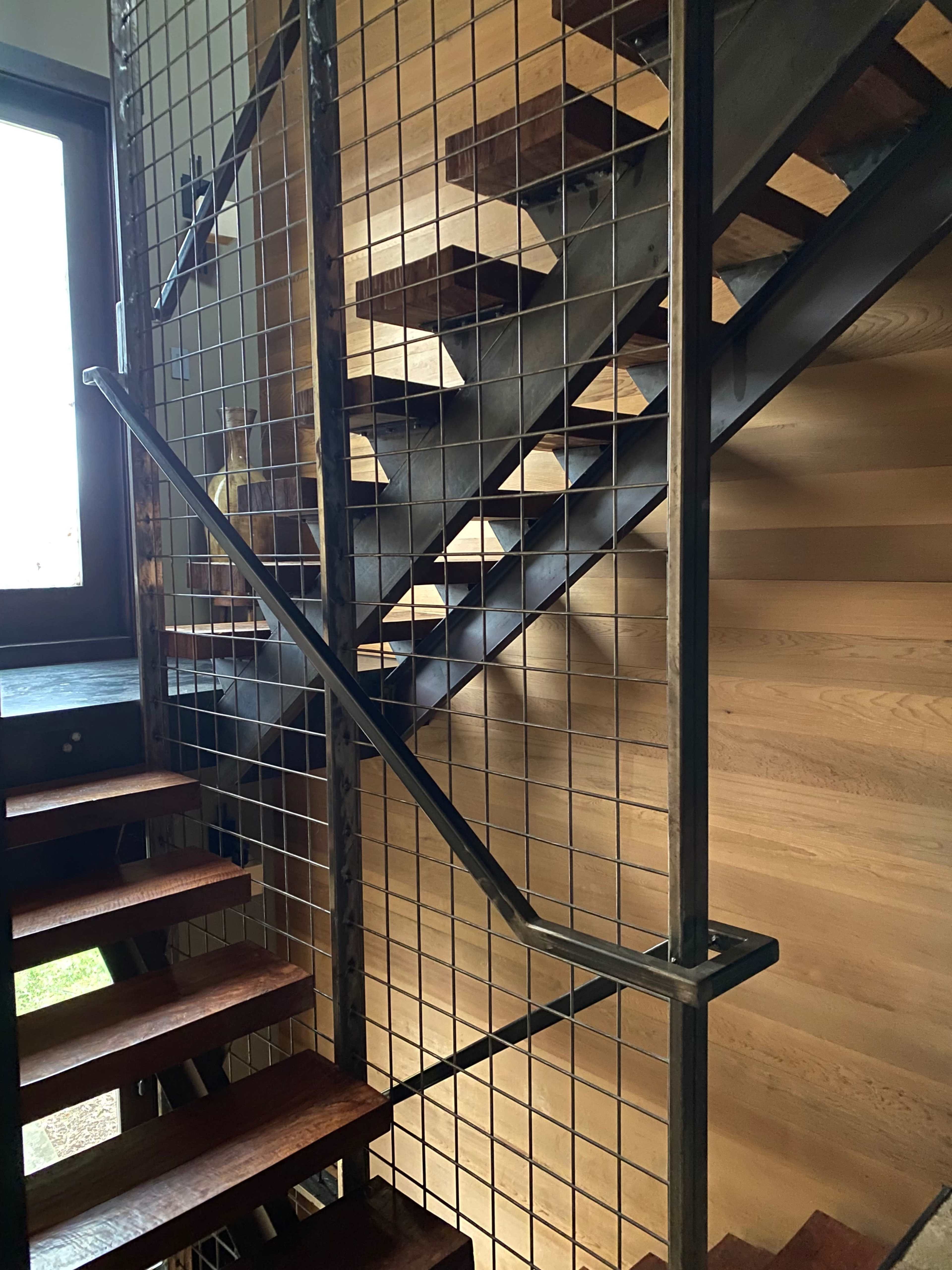 A modern staircase with wooden steps and metal railings, enclosed by a wire mesh guard.