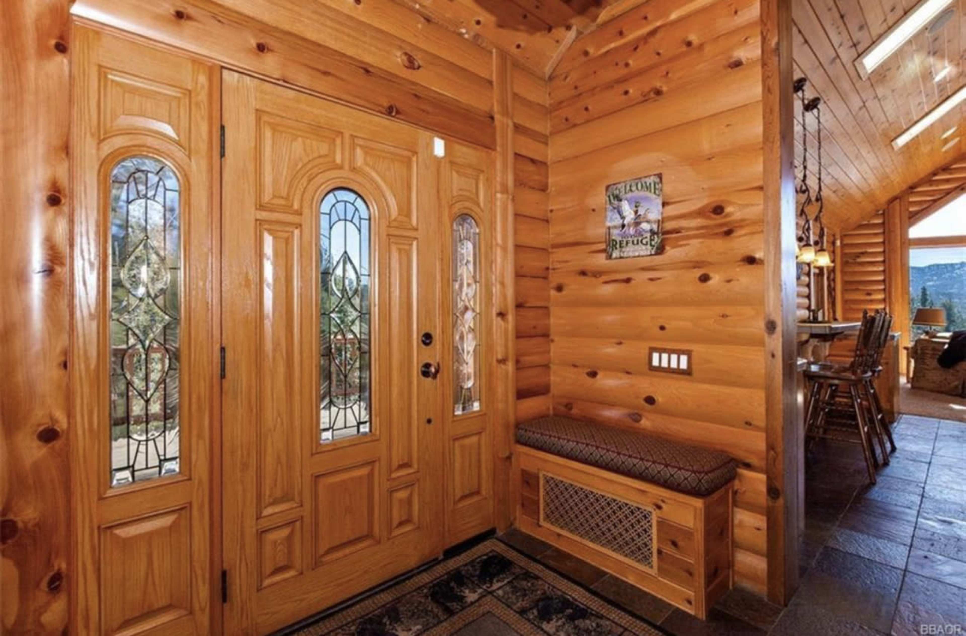 A log cabin entryway with double wooden doors featuring stained glass panels and a bench seat along the wall.