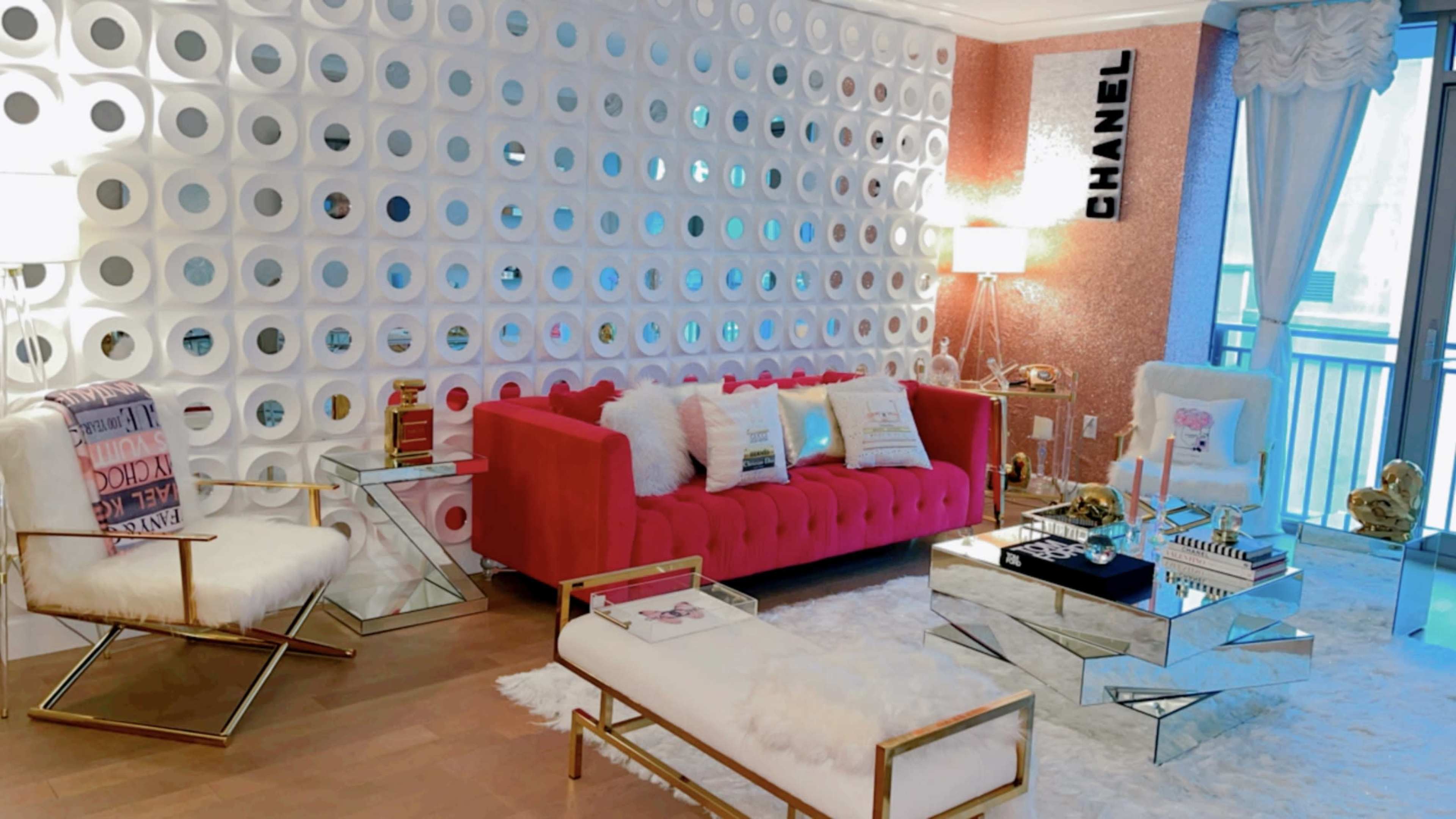 A stylish living room featuring a red tufted sofa, a white circular-patterned wall, and modern glass furniture.