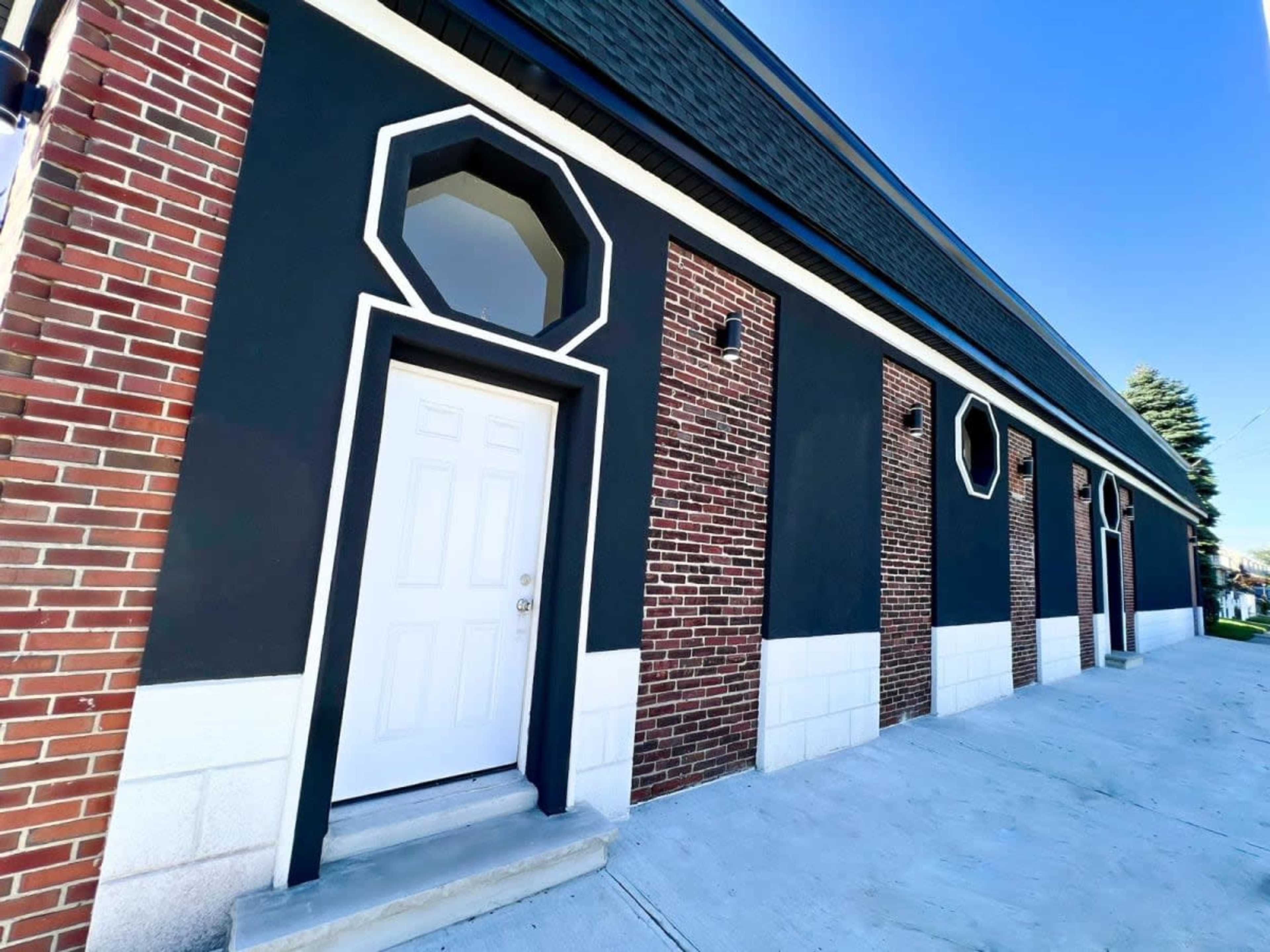 A building with a combination of textured brick and black painted walls, featuring multiple octagonal windows and a white front door.