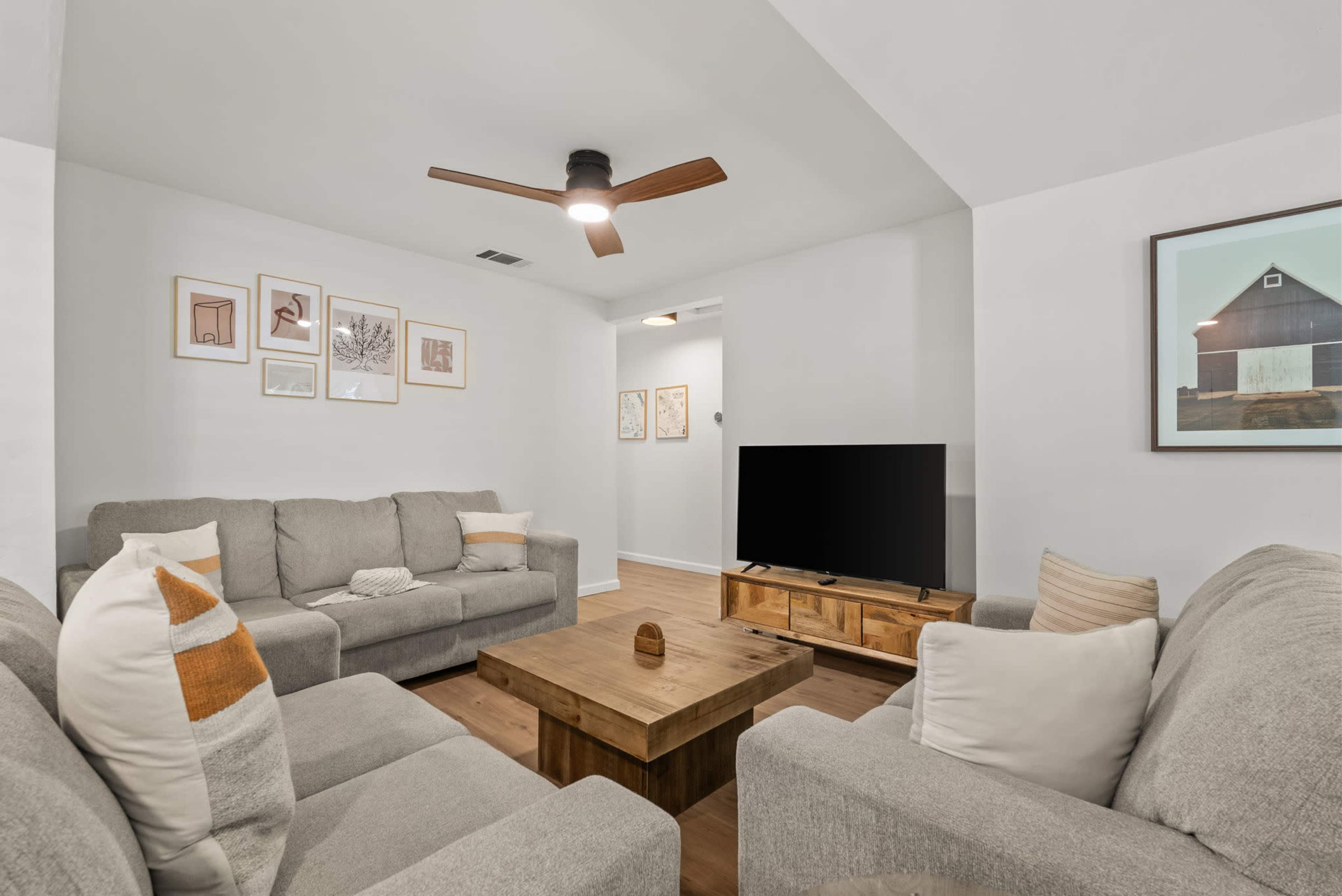 A cozy living room features two grey sofas, a wooden coffee table, a television on a wooden stand, and wall art displayed in frames.