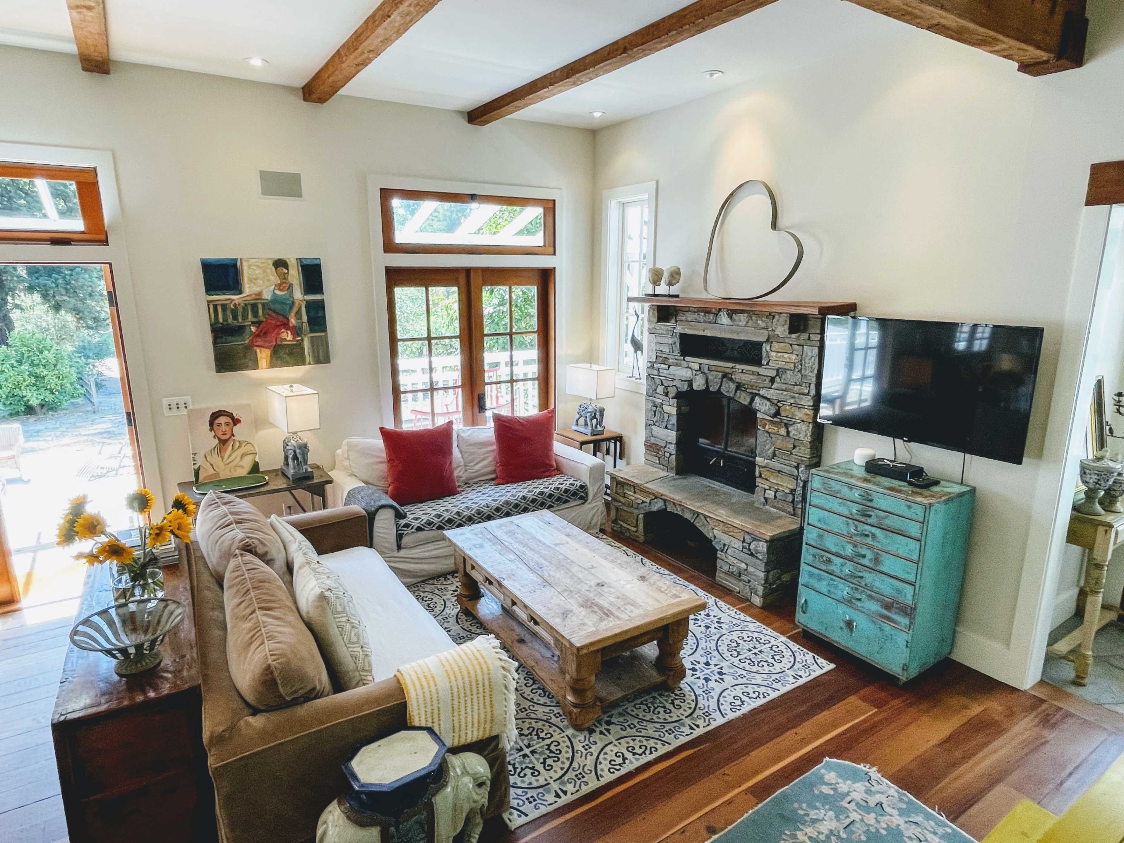 The living room features a beige couch, a wooden coffee table, and a stone fireplace, with large windows that allow natural light to flood the space.