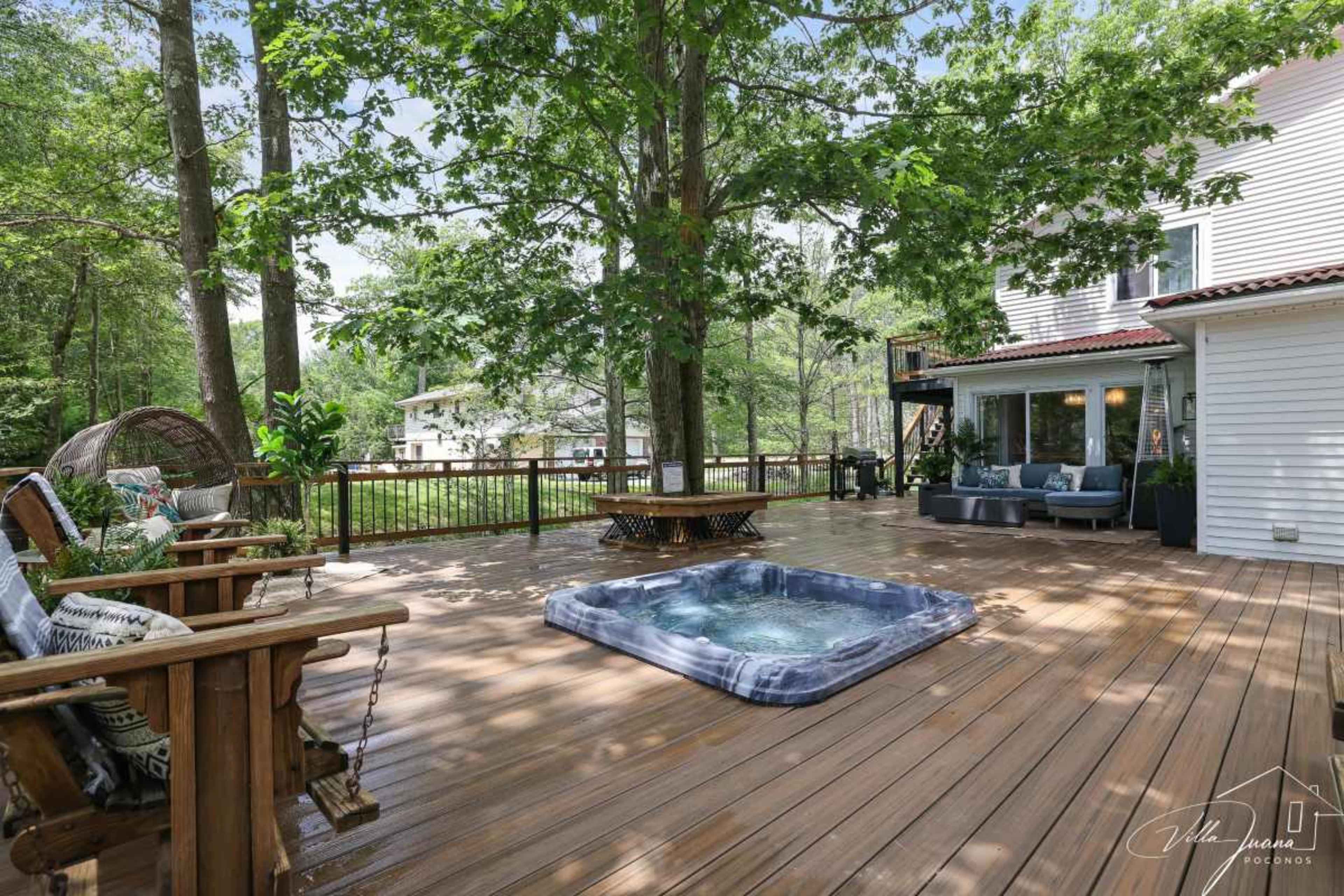 A wooden deck surrounded by trees features a hot tub and comfortable seating areas.