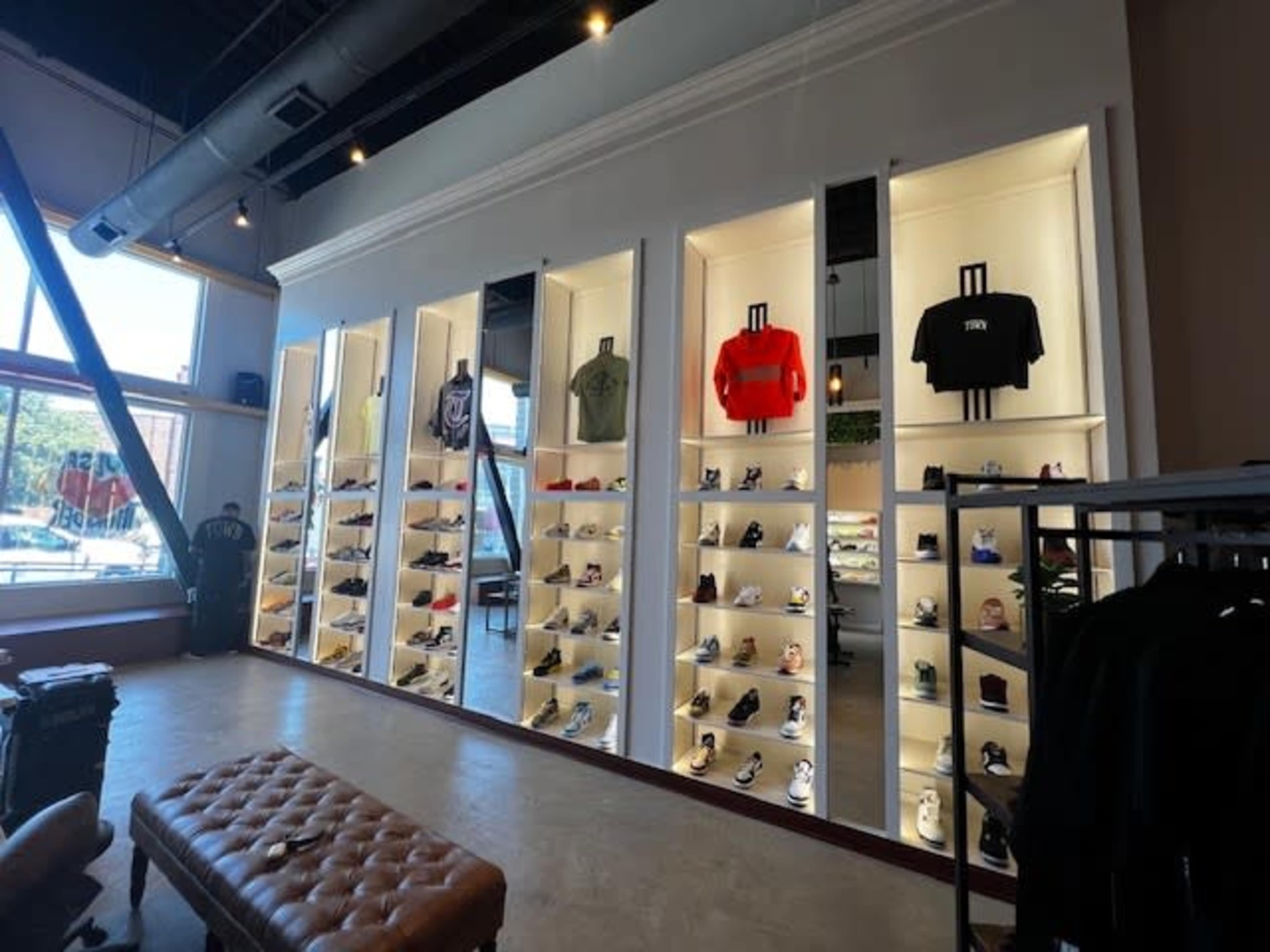 A retail space features illuminated display shelves showcasing various sneakers and apparel, arranged on a white wall with mirrors.