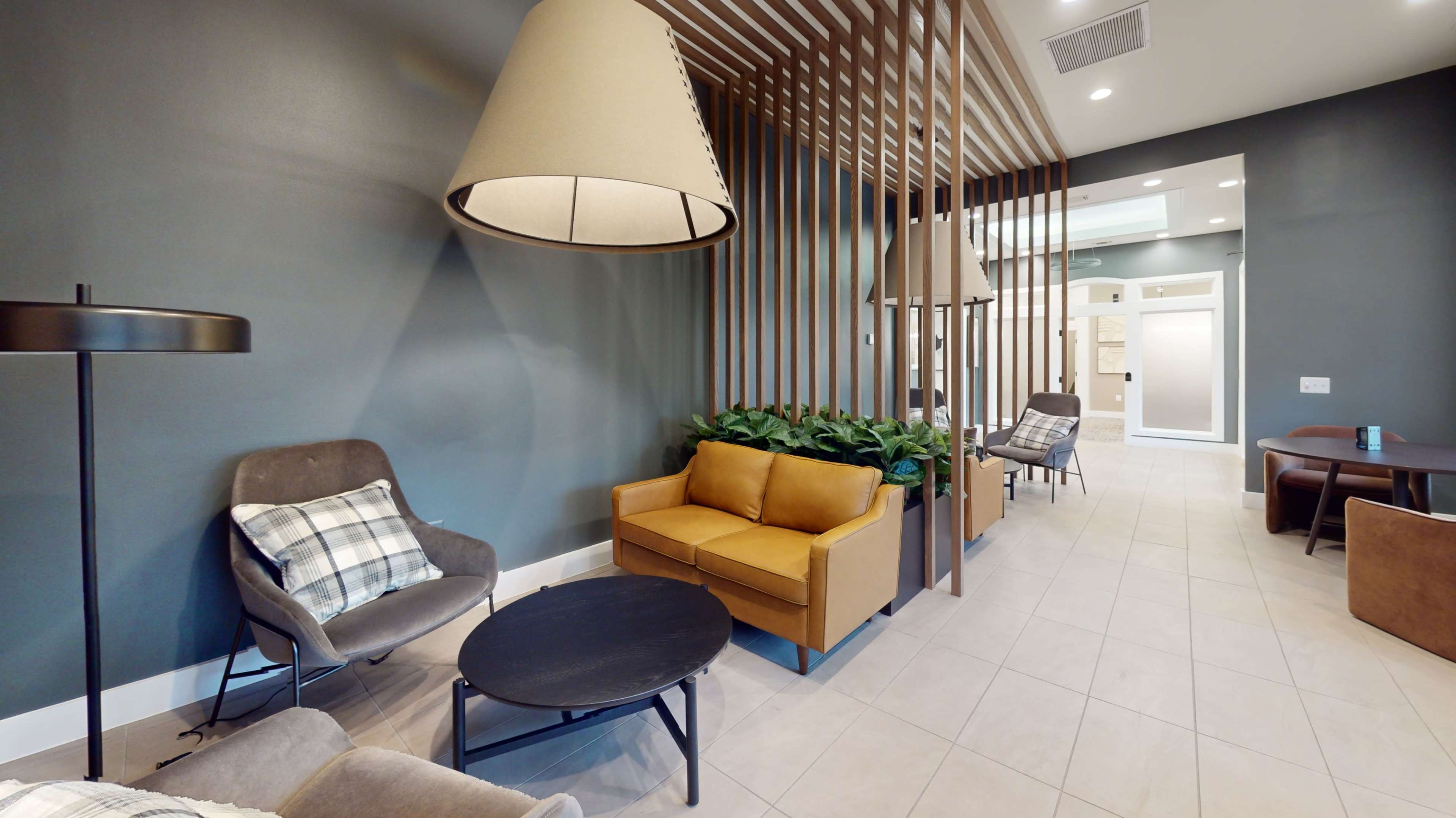 A modern lounge area featuring a yellow couch, gray armchairs, and decorative plants, with unique light fixtures and wooden paneling decor.