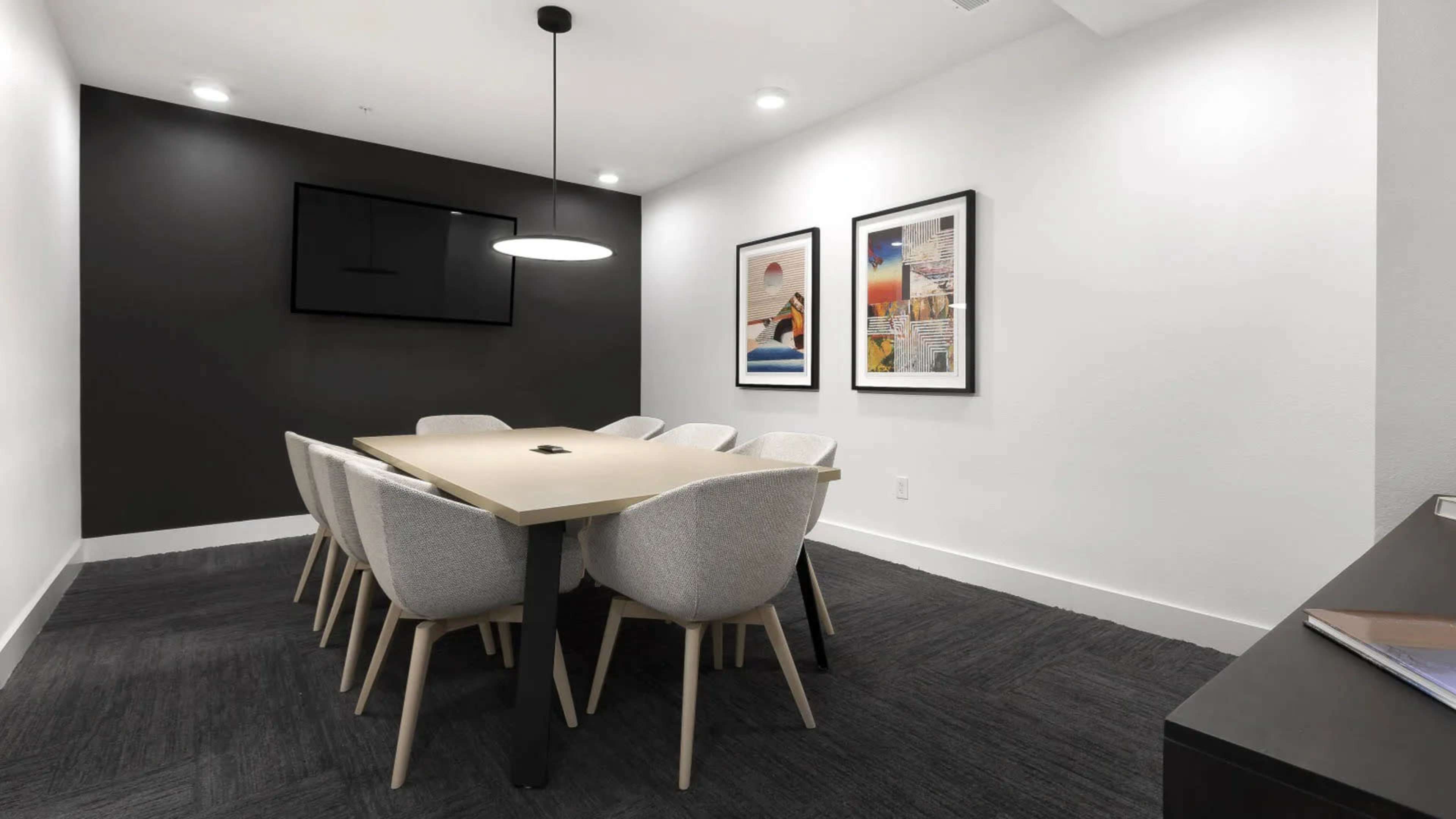 A modern conference room with a long table surrounded by eight upholstered chairs, flanked by black and white walls and two framed artworks.