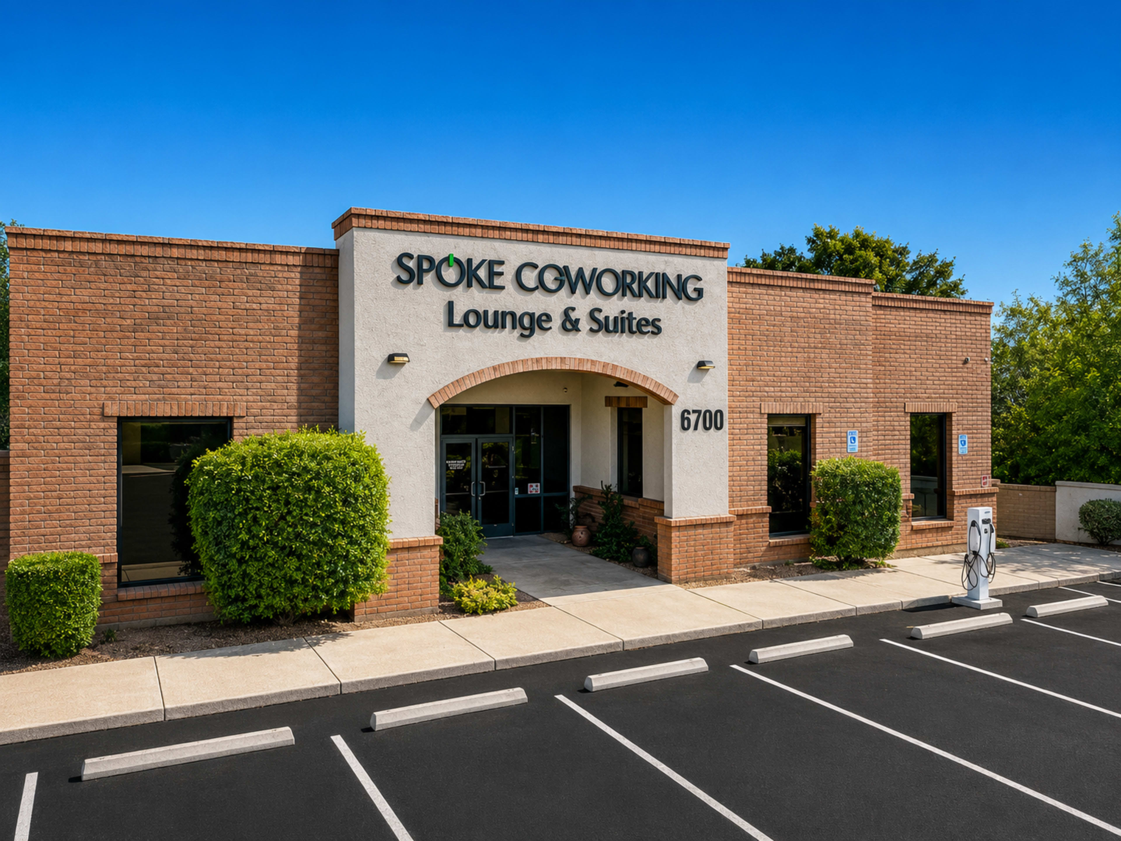 The image shows the exterior of a building labeled "Spoke Coworking Lounge & Suites," featuring a brick facade and clear blue skies above.
