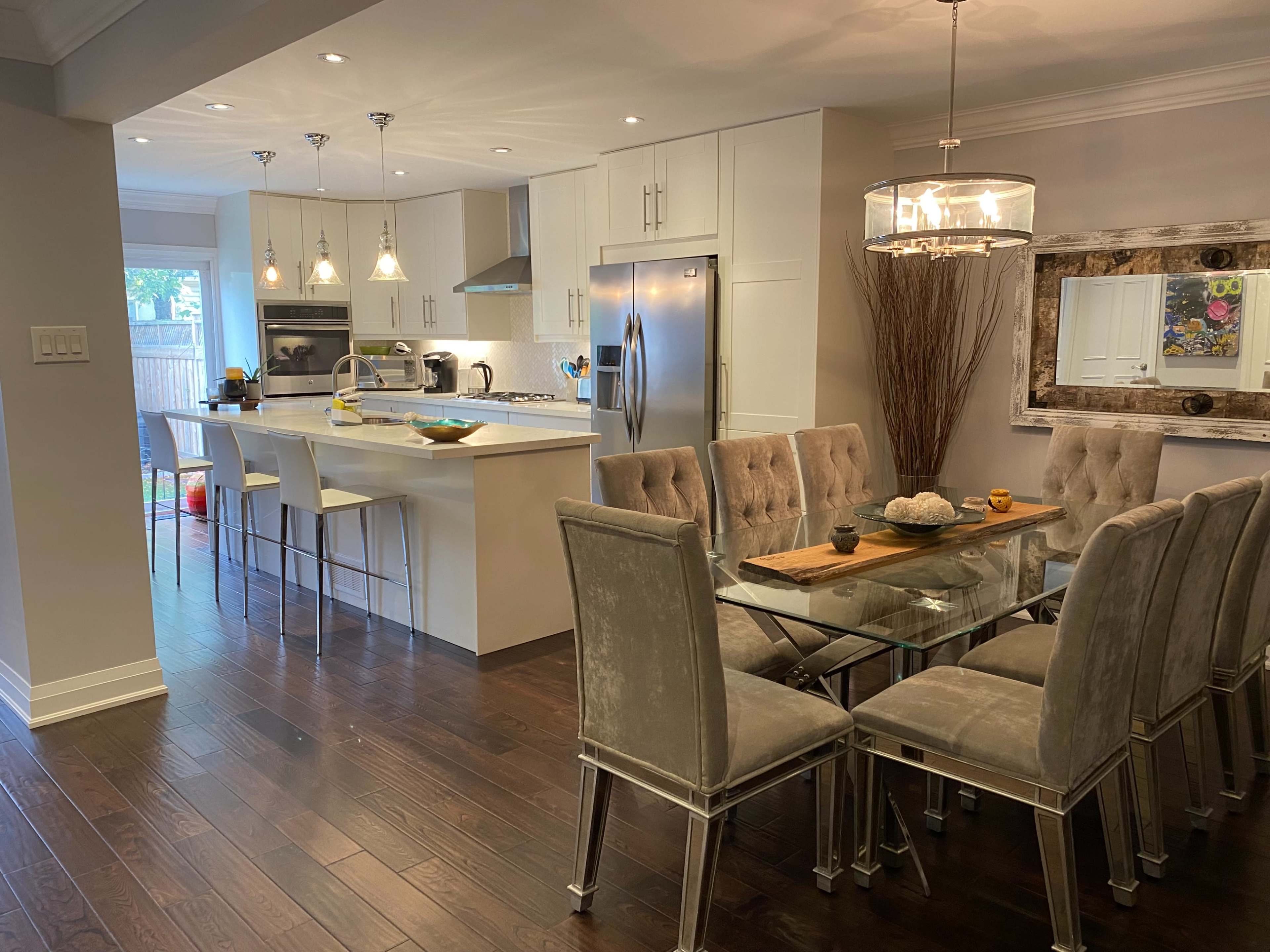 A modern kitchen and dining area with a glass dining table set for eight and a sleek kitchen with stainless steel appliances.