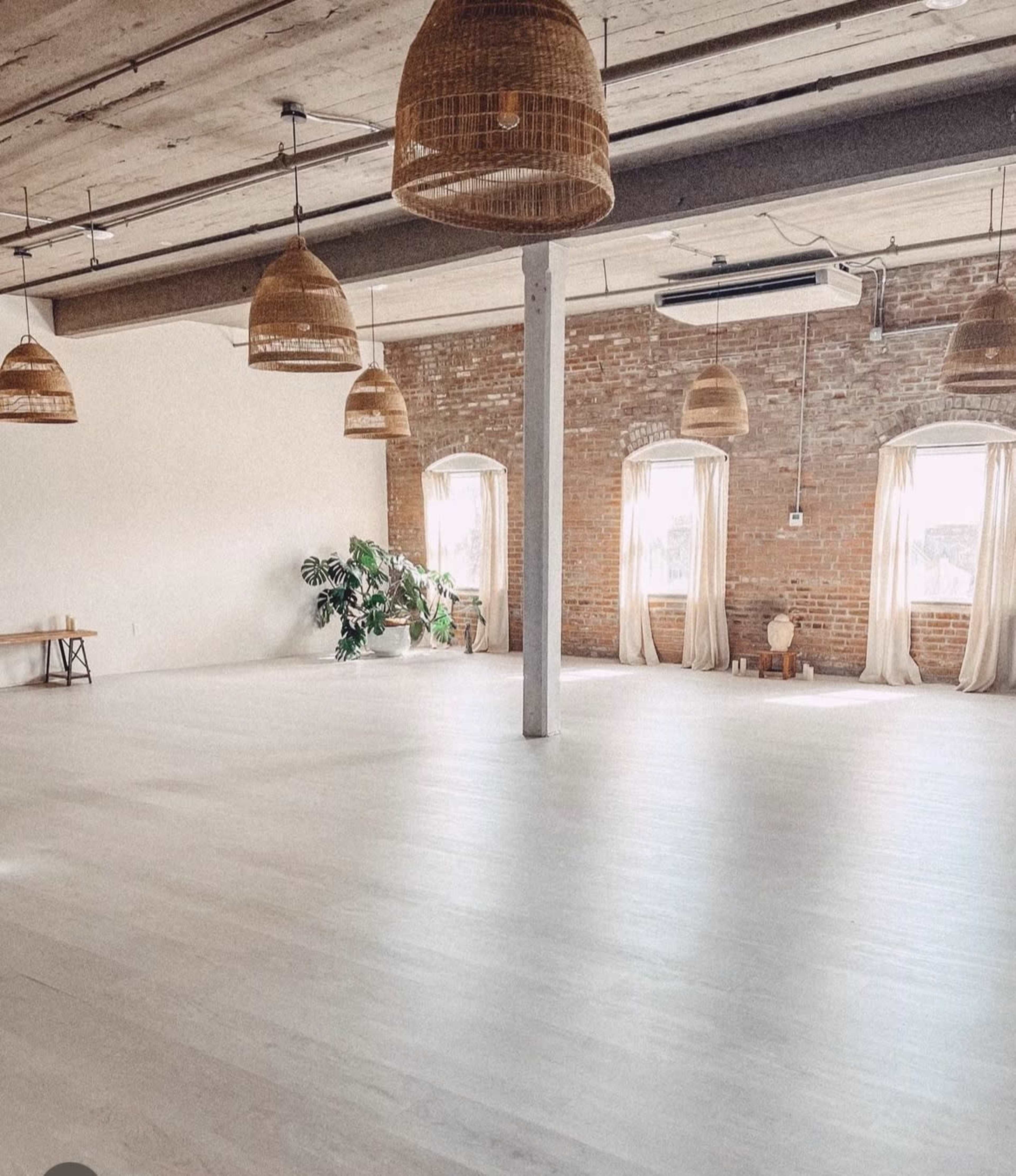 A spacious, lightly furnished room with wooden floors, large windows, and hanging wicker light fixtures.