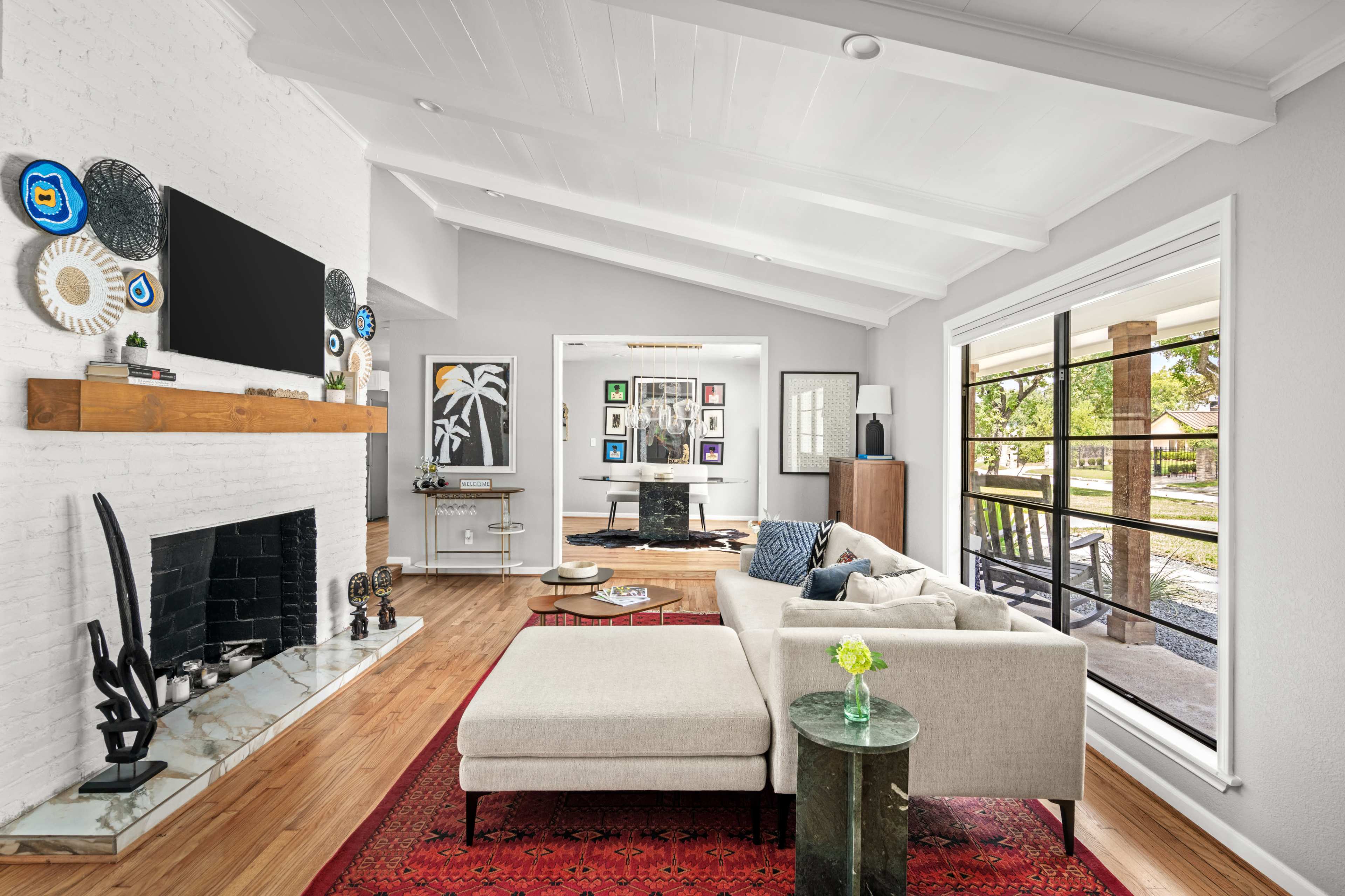 The image depicts a modern living room with a white-brick fireplace, a large sectional sofa, and decorative artwork on the walls.