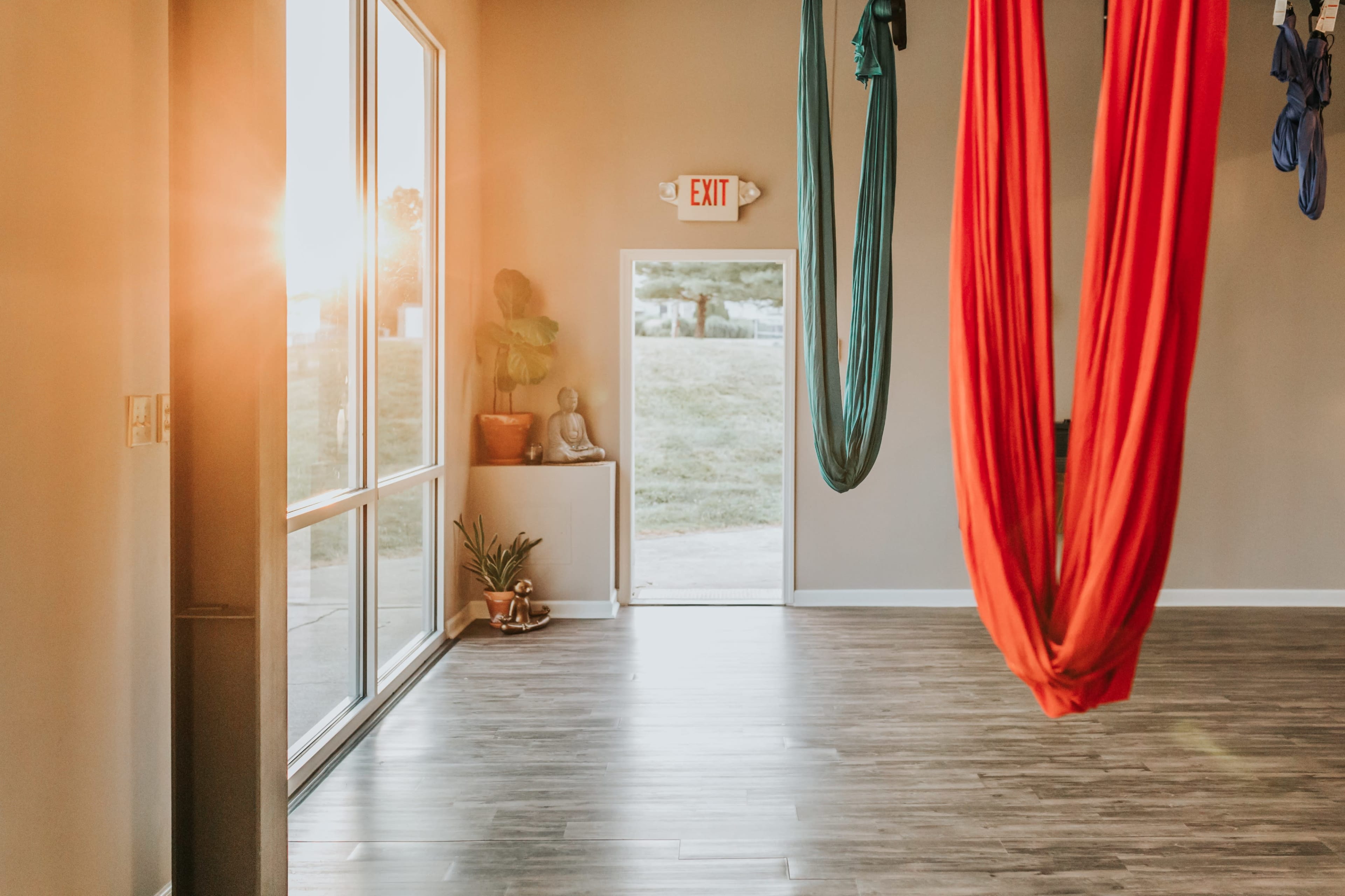 An aerial yoga studio with red and blue fabric hammocks hanging from the ceiling, and sunlight streaming through large windows.