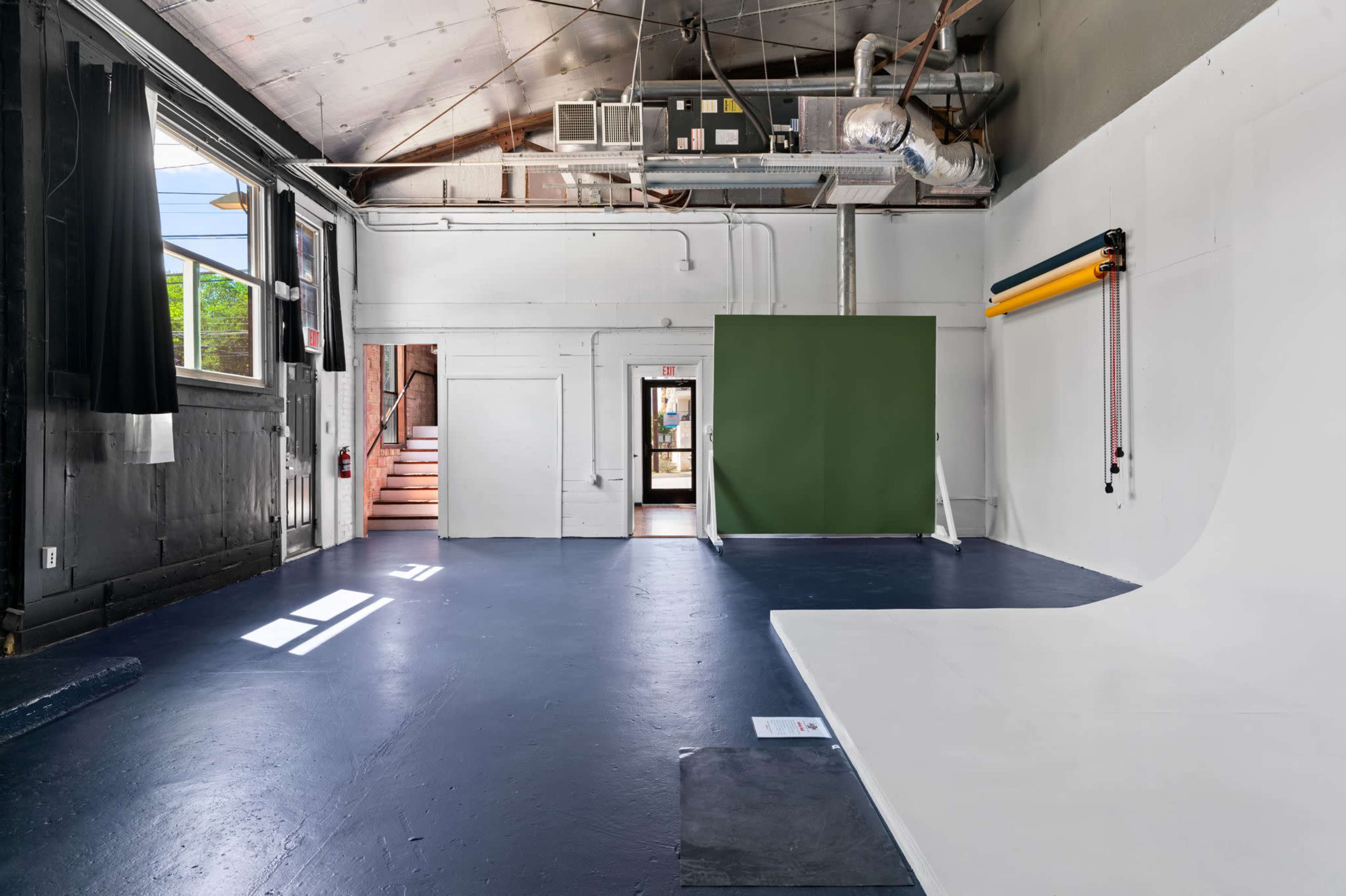 An empty studio space with a white backdrop and a green wall, featuring large windows that illuminate the area.