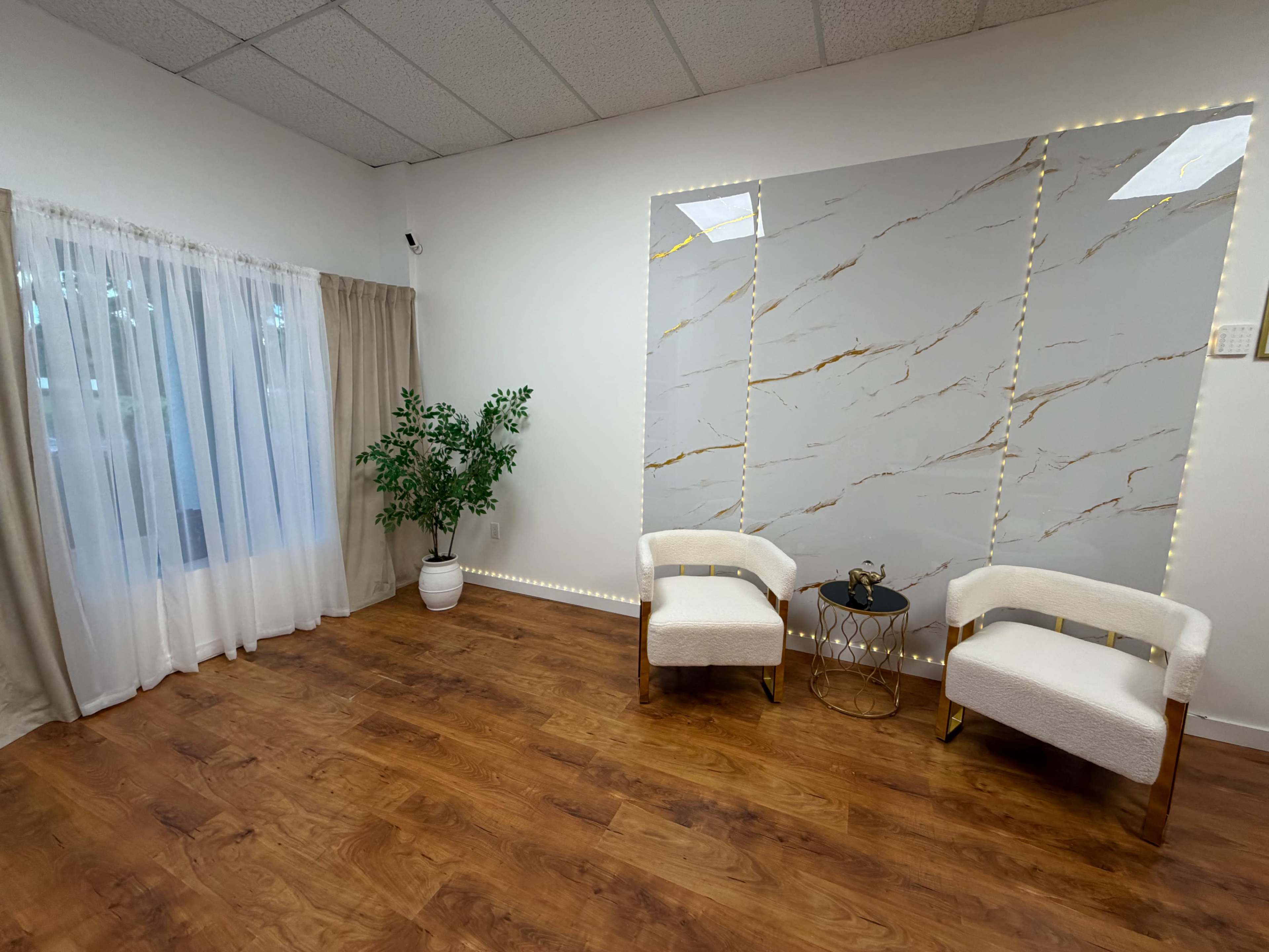 The interior features two white chairs positioned next to a small table, with a decorative plant in a pot and a large marble wall as a backdrop.