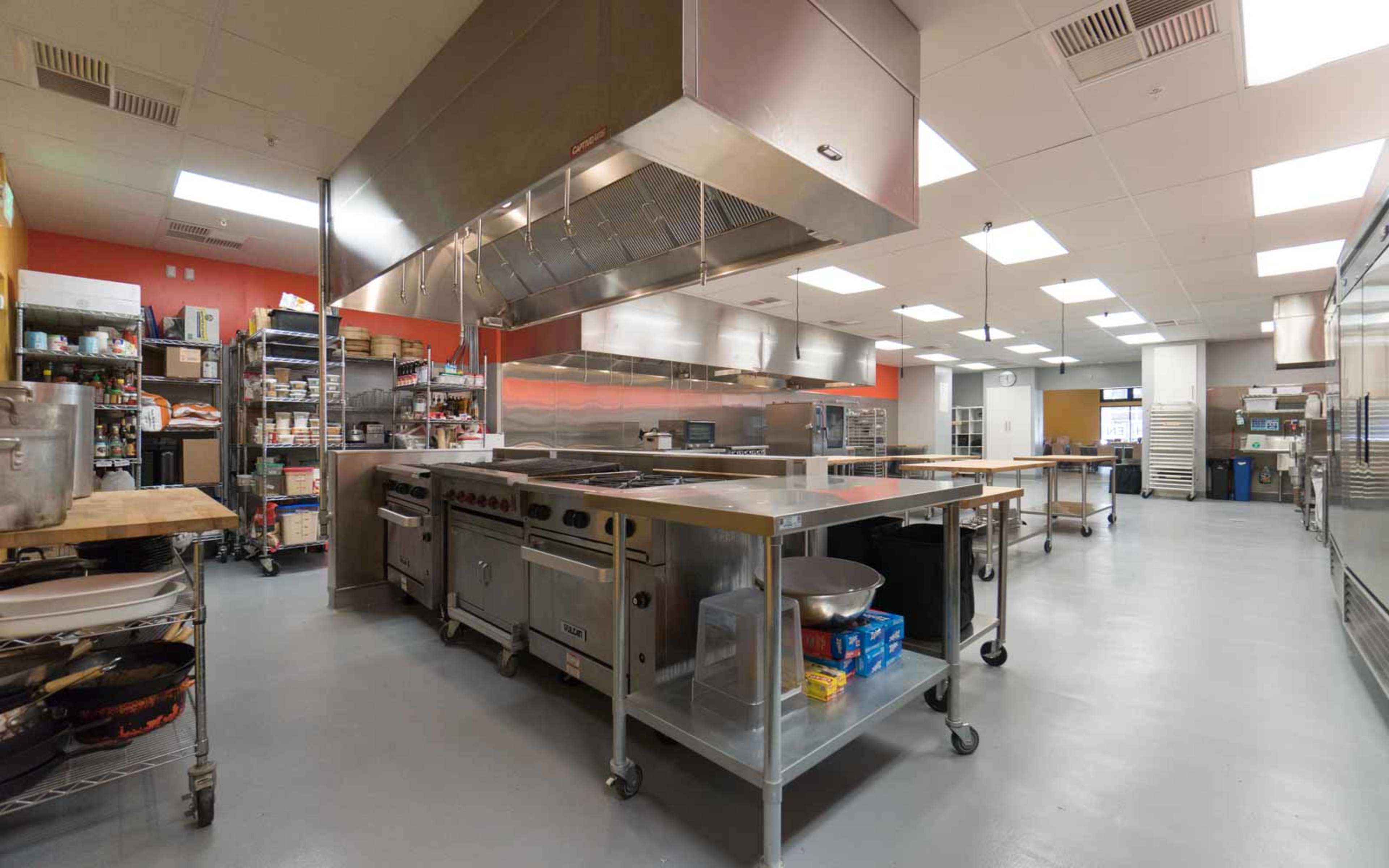 A spacious commercial kitchen with stainless steel equipment, worktables, and neatly organized storage areas.