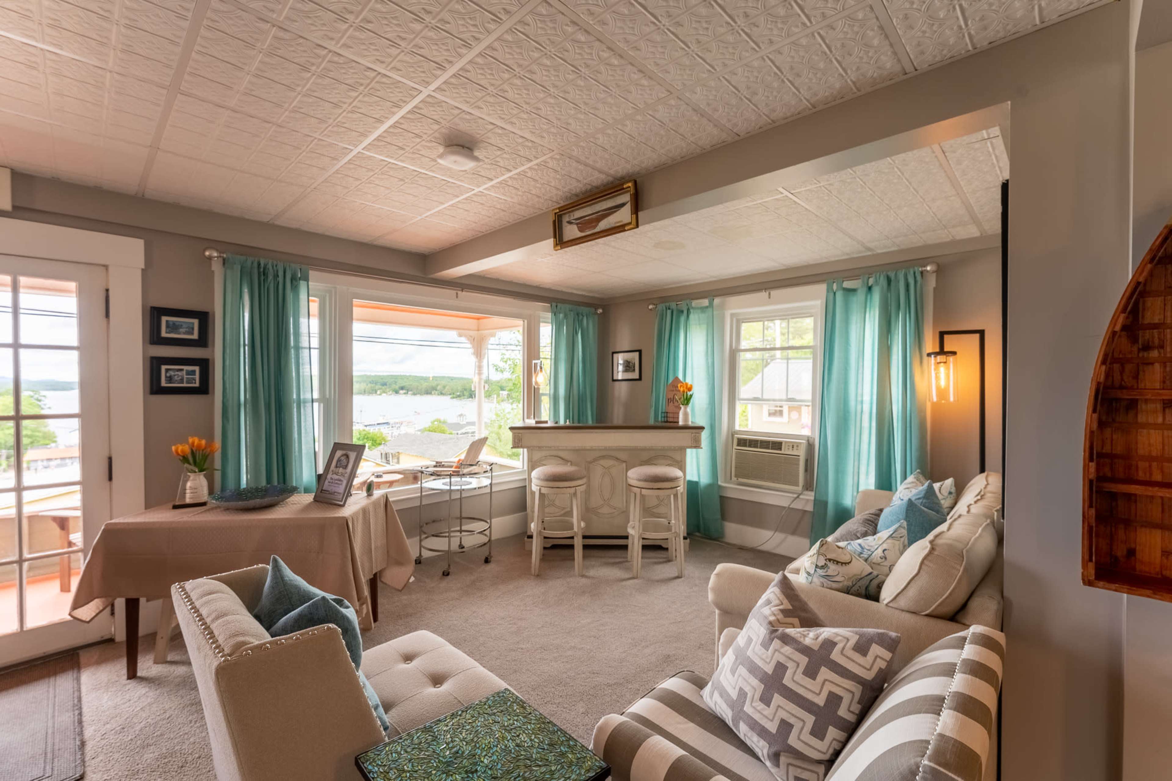 A cozy living area with a light-colored sofa, turquoise curtains, and a bar area overlooking a view.