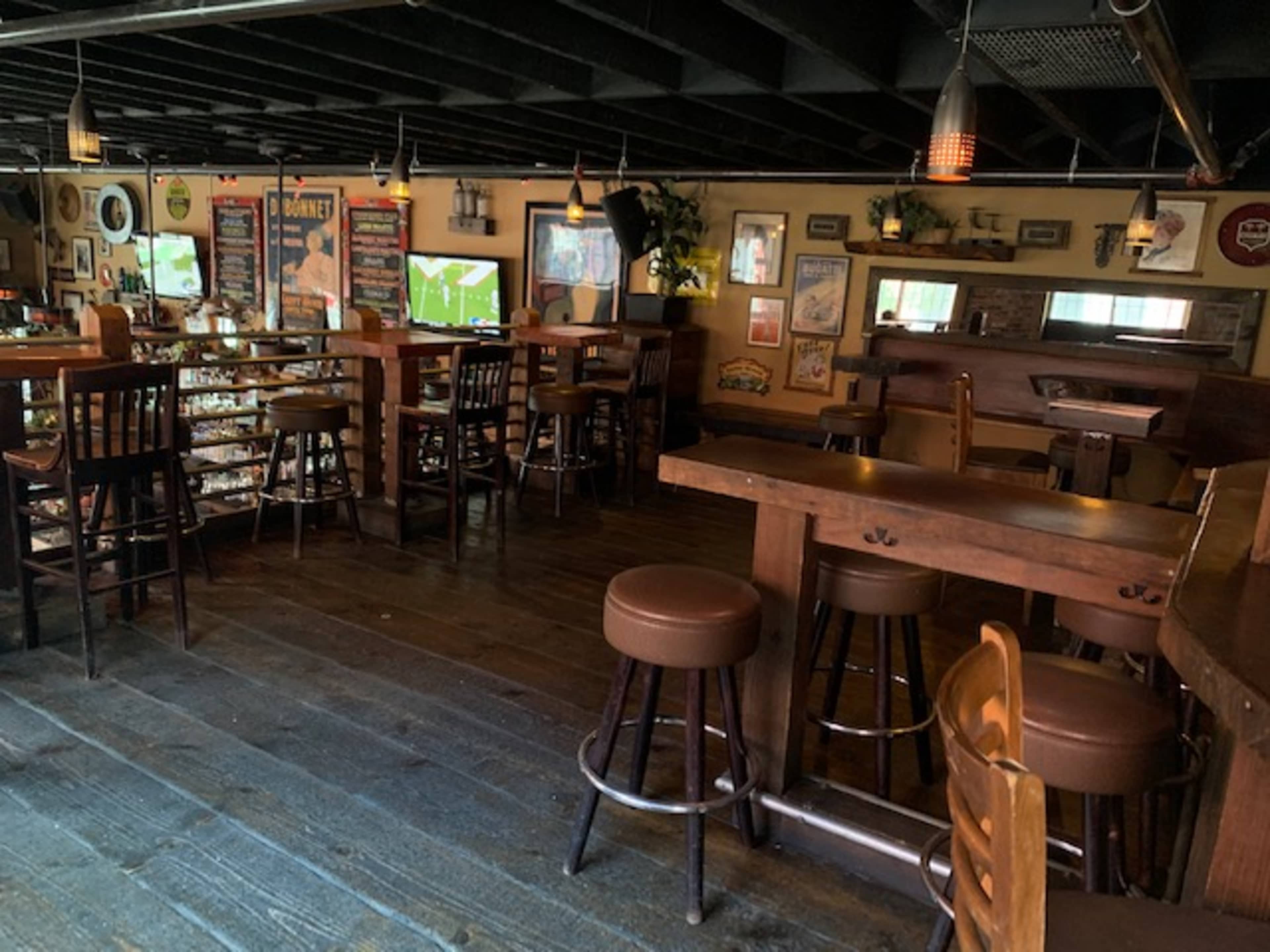 The interior of a rustic bar with wooden tables and chairs, dim lighting, and vintage decorations on the walls.