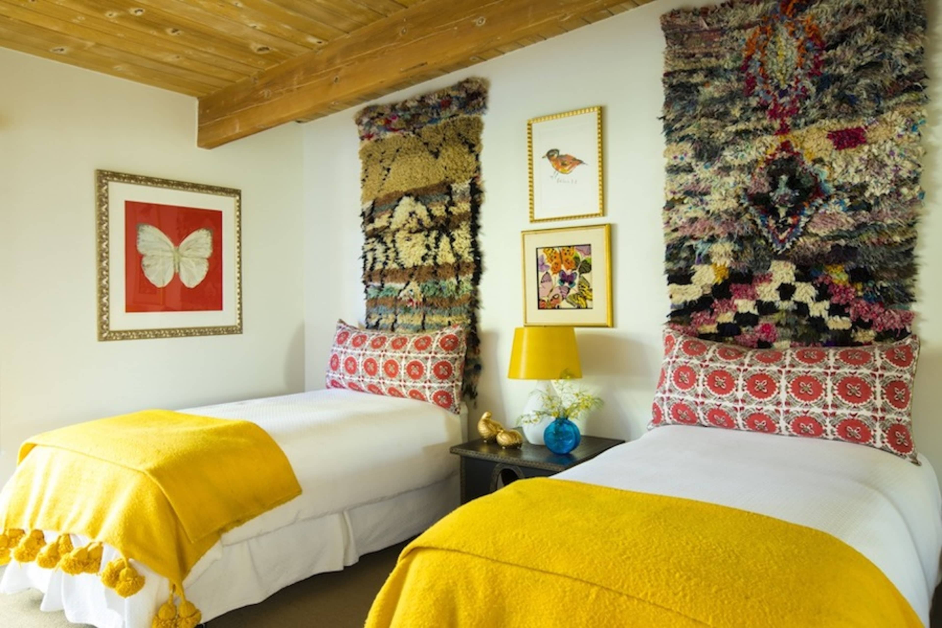 A brightly decorated bedroom featuring two twin beds with yellow throw blankets and colorful wall hangings.