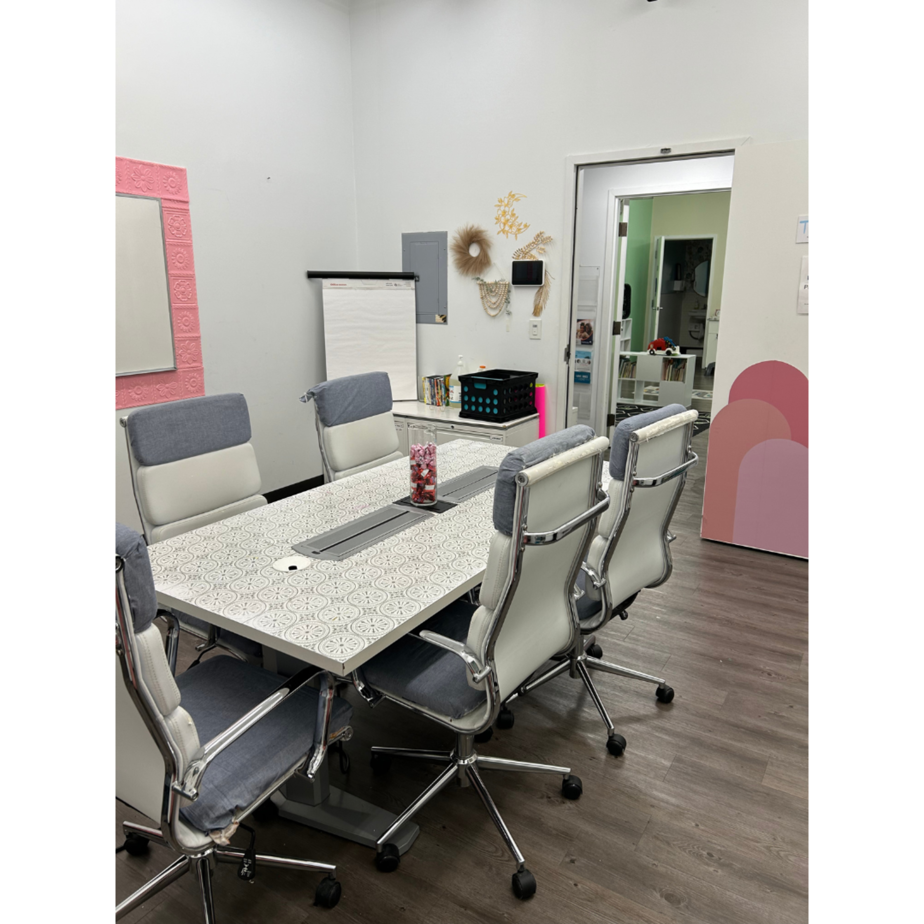 The image shows a modern conference room with a patterned table surrounded by six light-colored office chairs and various decorative elements on the walls.