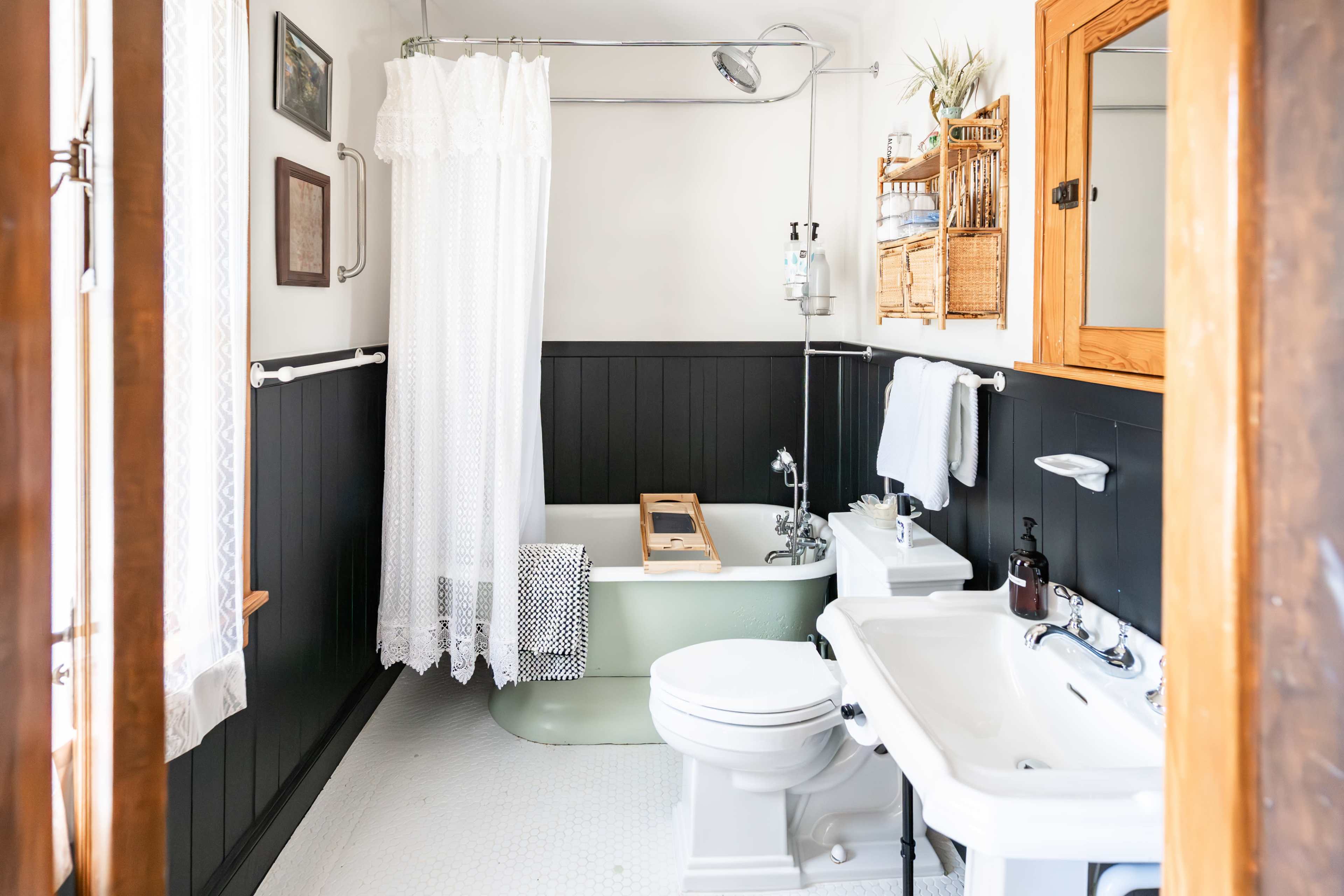 The bathroom features a vintage bathtub with a shower curtain, a sink with a mirror, and a combination of dark and light wall paneling.