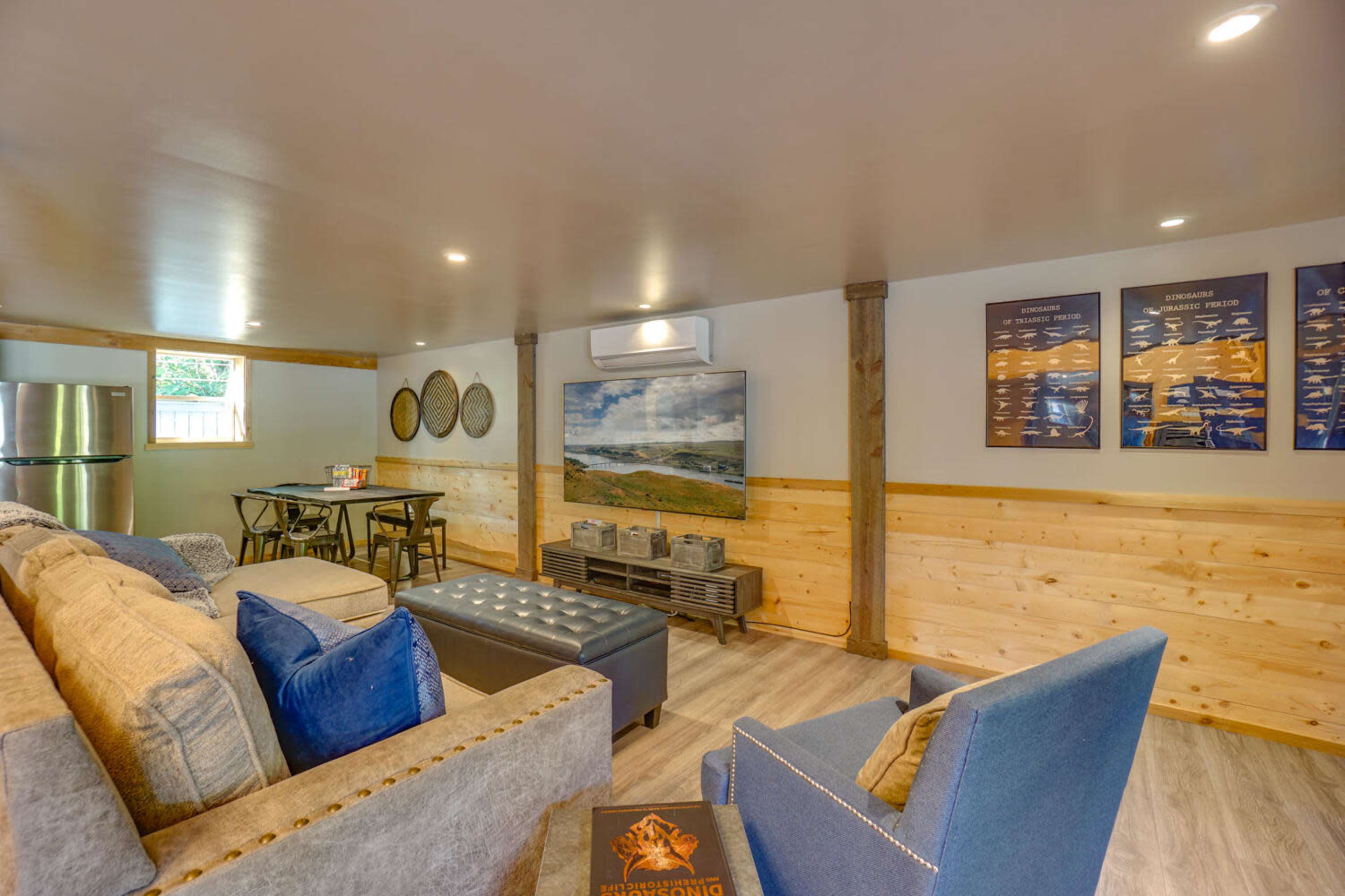 The image shows a cozy basement living area with a sofa, a dining table, and a wall-mounted TV, featuring wood paneling and modern decor.