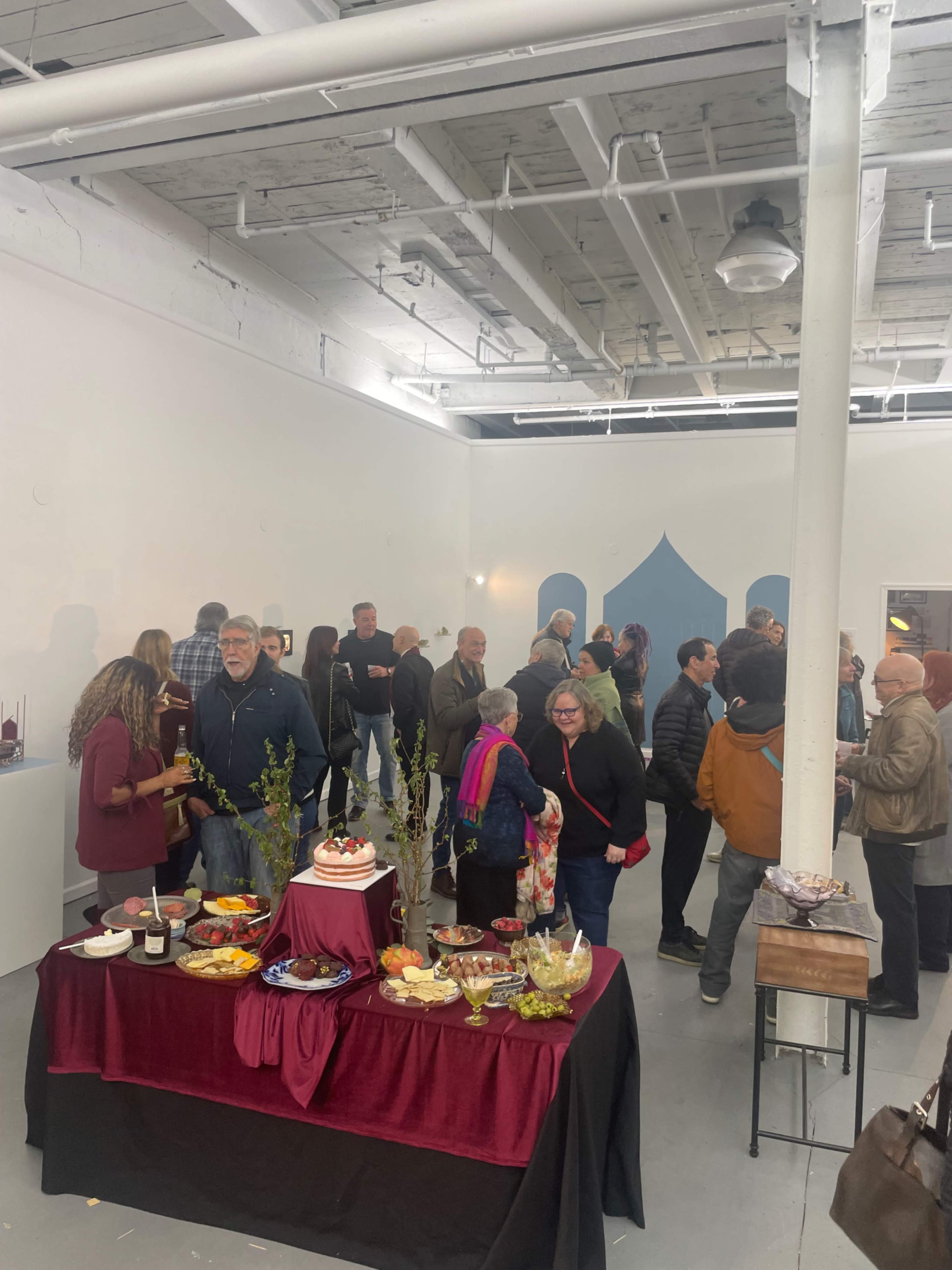 A group of people gathers around a table filled with various food items in a spacious event space.