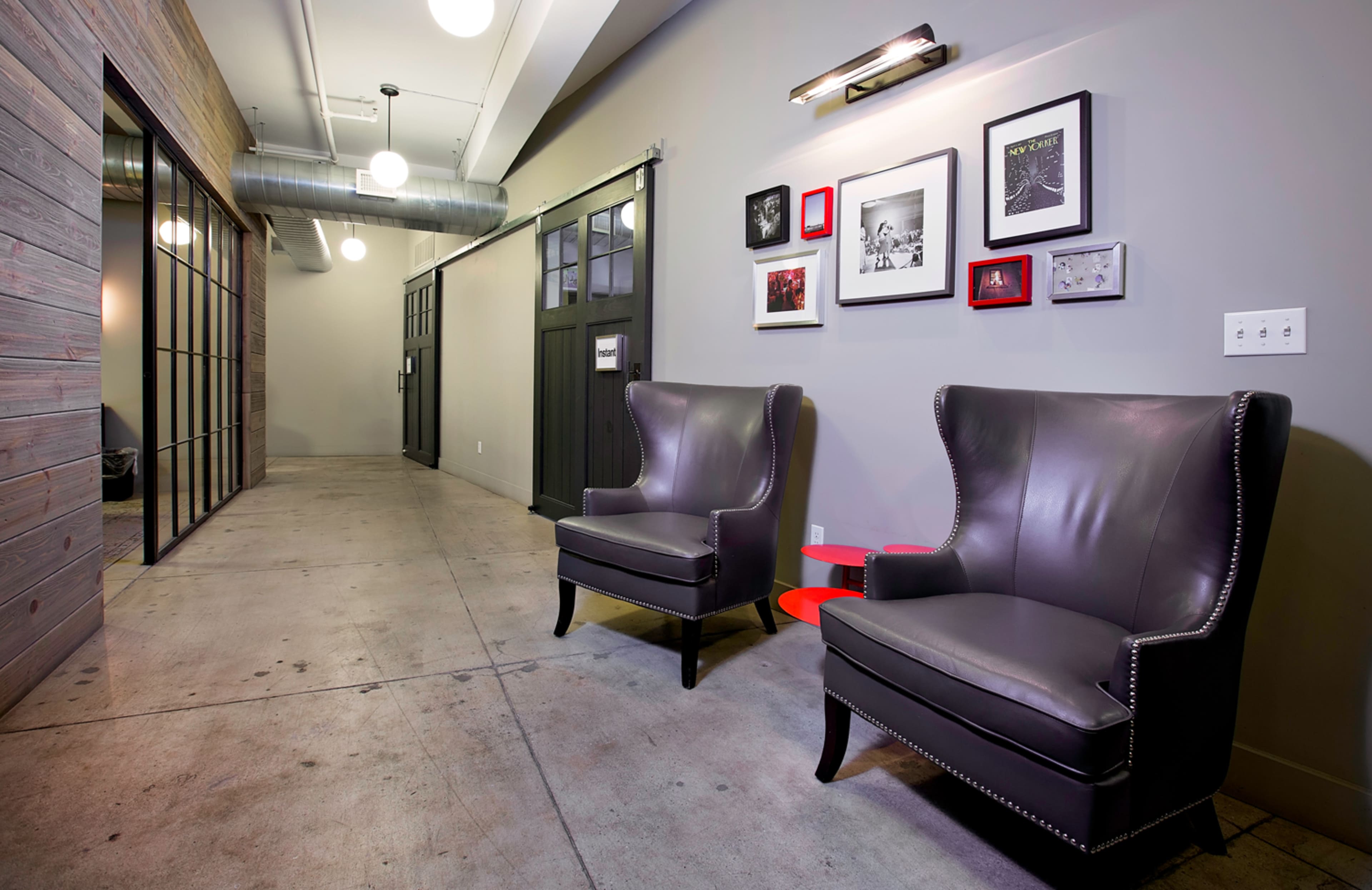 The image shows a modern hallway with two black leather armchairs facing a wall adorned with framed black-and-white photographs.