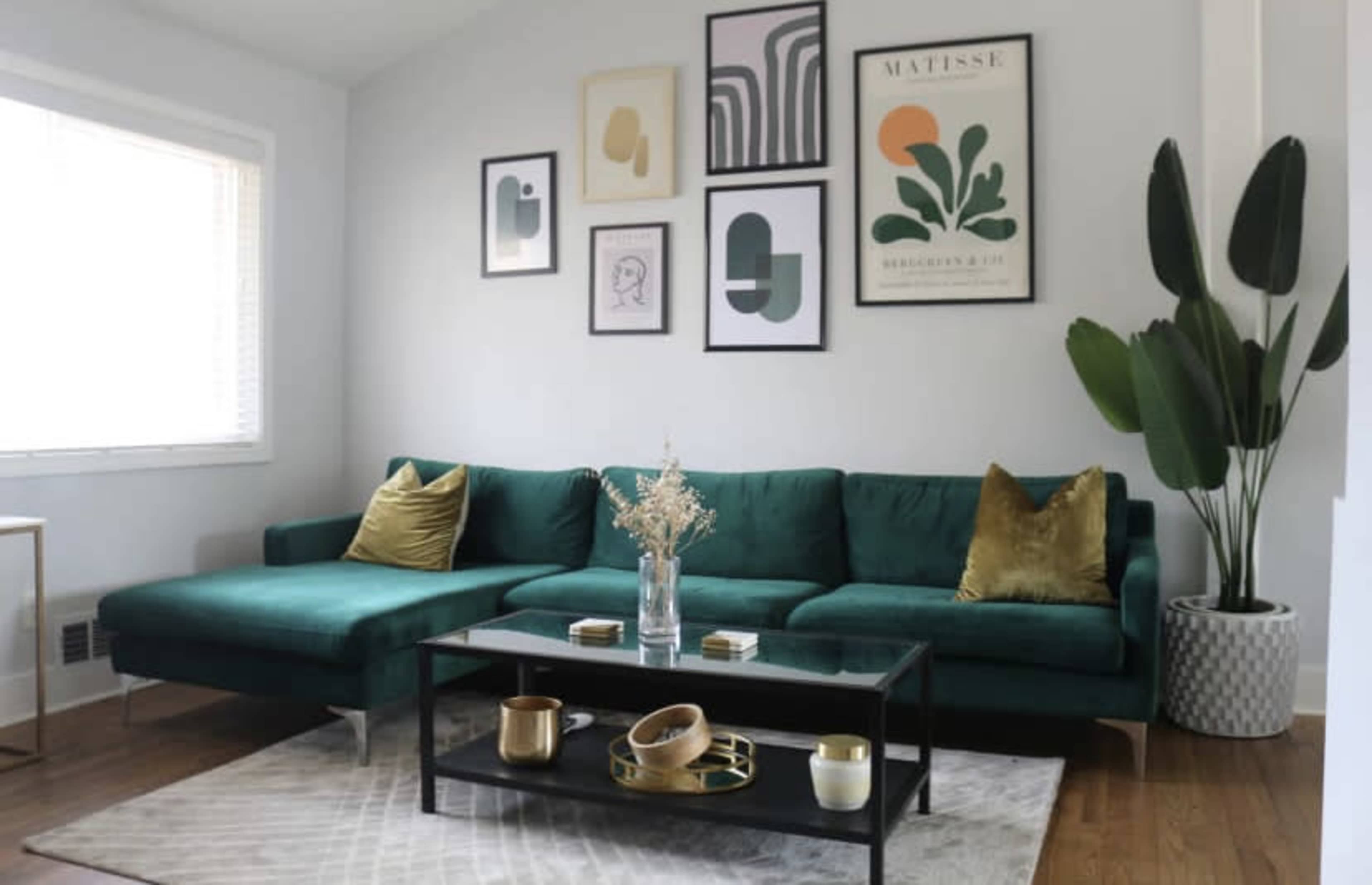 The image shows a modern living room with a green sectional sofa, decorative wall art, and a coffee table on a patterned rug.